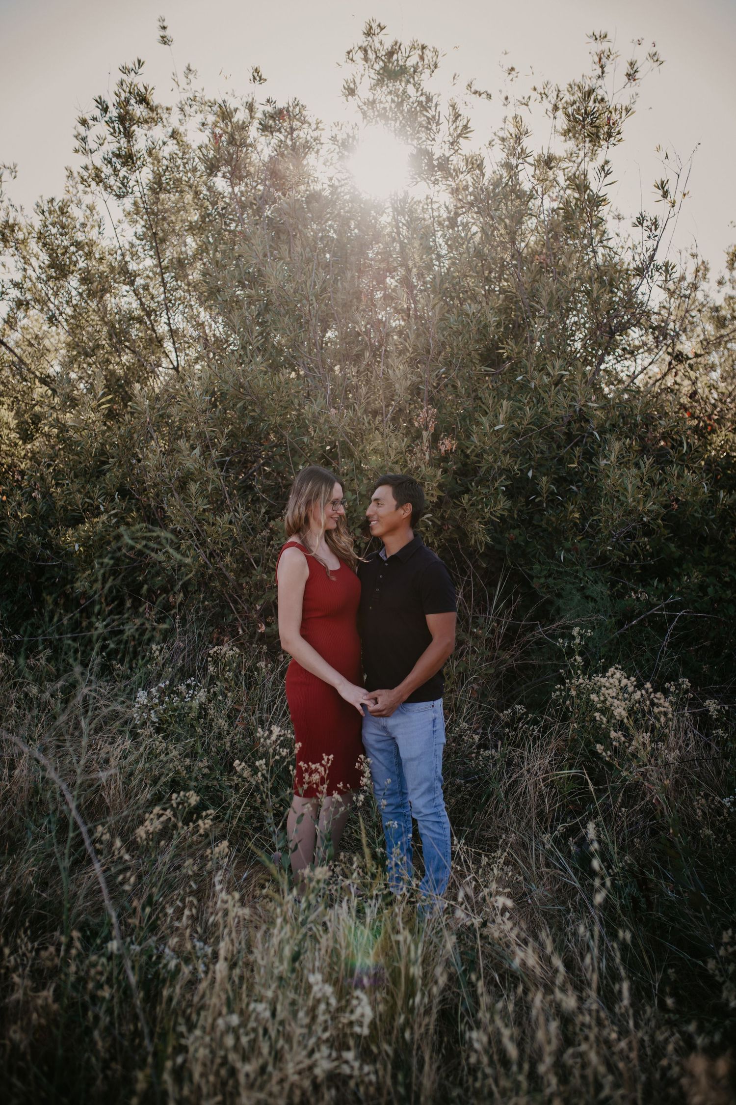 A couple poses intimately against natural foliage during golden hour.