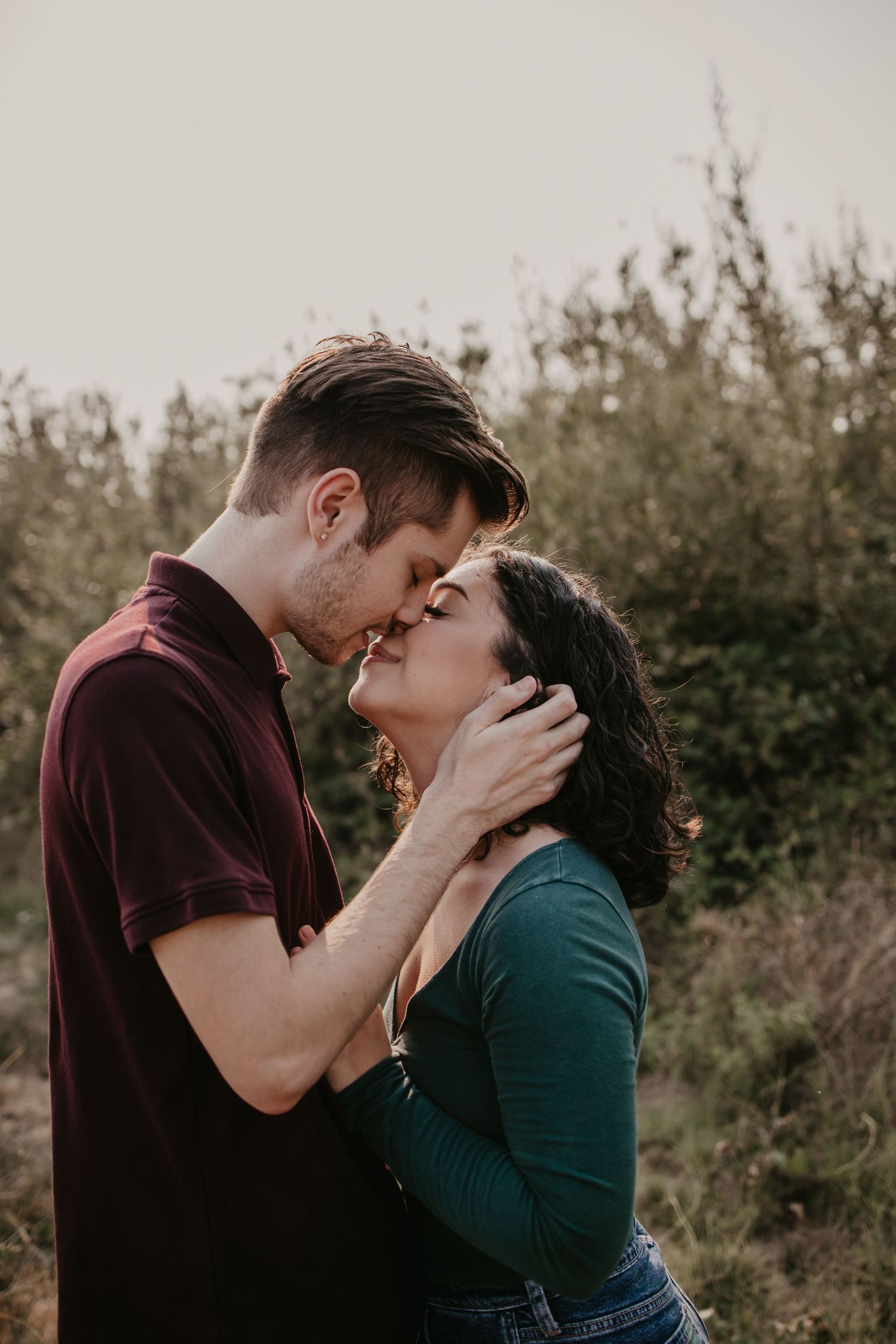 An intimate portrait of a couple sharing a tender moment against natural foliage.