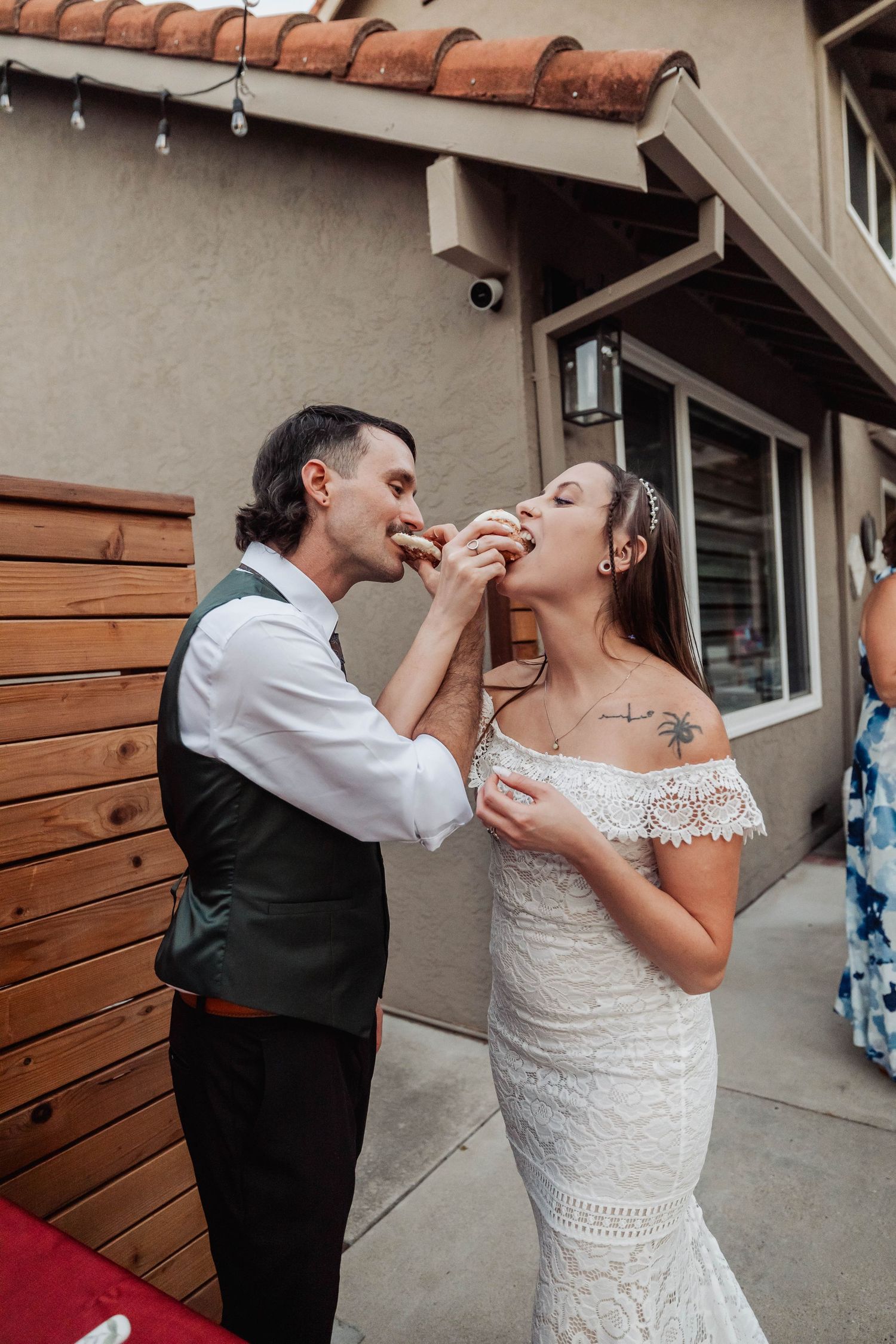 Wedding couple sharing cake during their reception outside a stucco building.