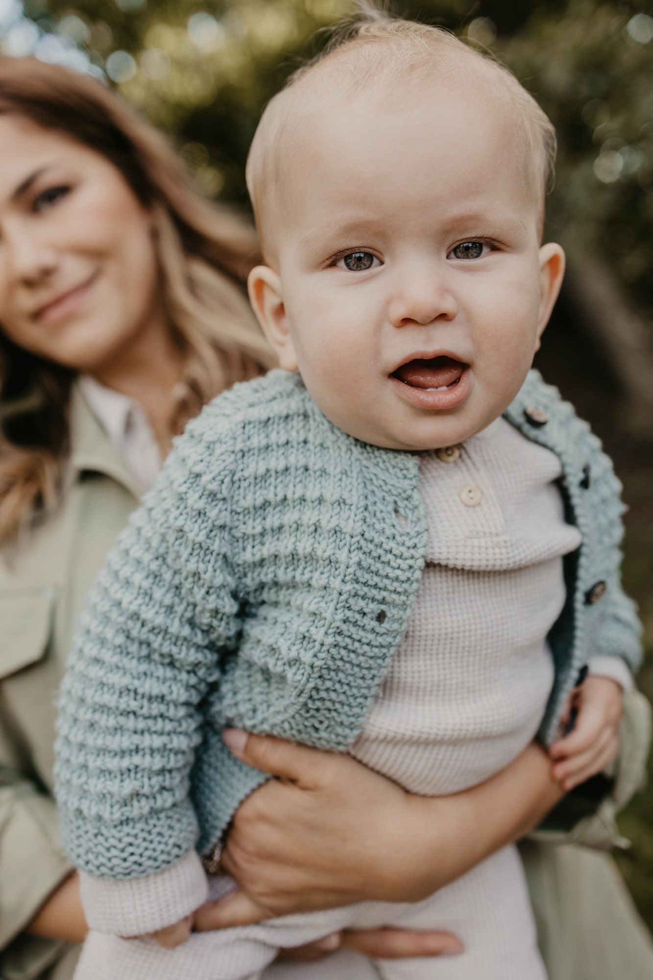Portrait of cheerful baby in gray knit sweater against blurred natural background.
