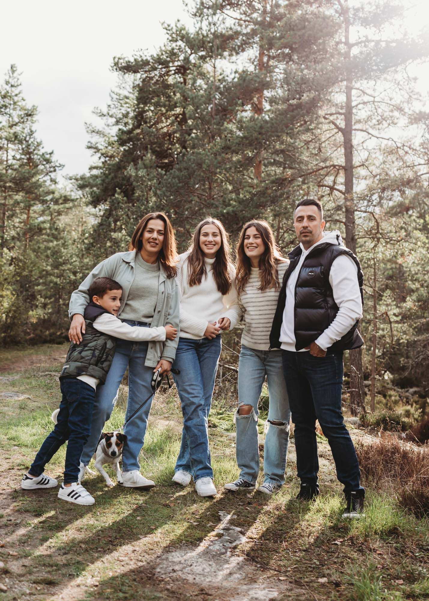 A cheerful family group poses together on a forest trail with matching casual outfits.