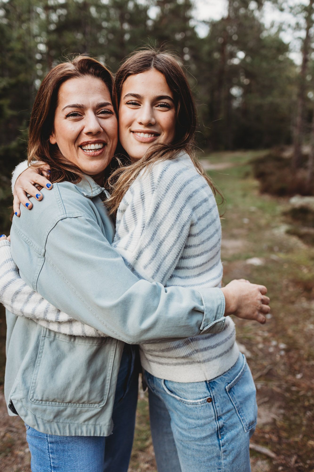 Two people sharing a warm embrace while wearing casual outerwear in a natural outdoor setting.