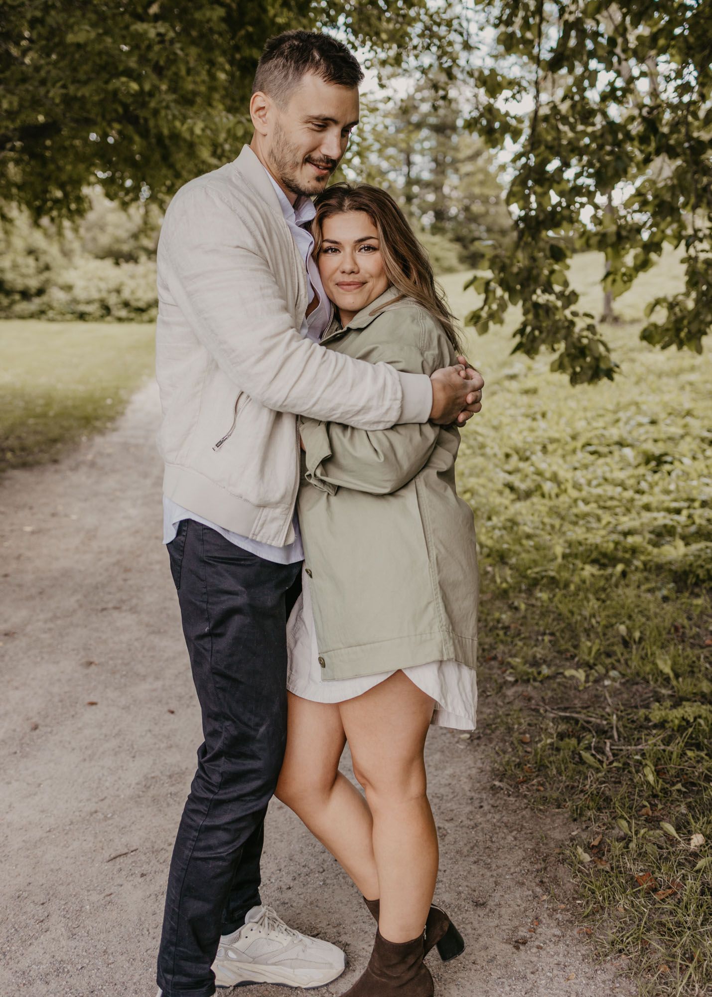 A couple shares a tender moment while standing on a dirt path in nature.
