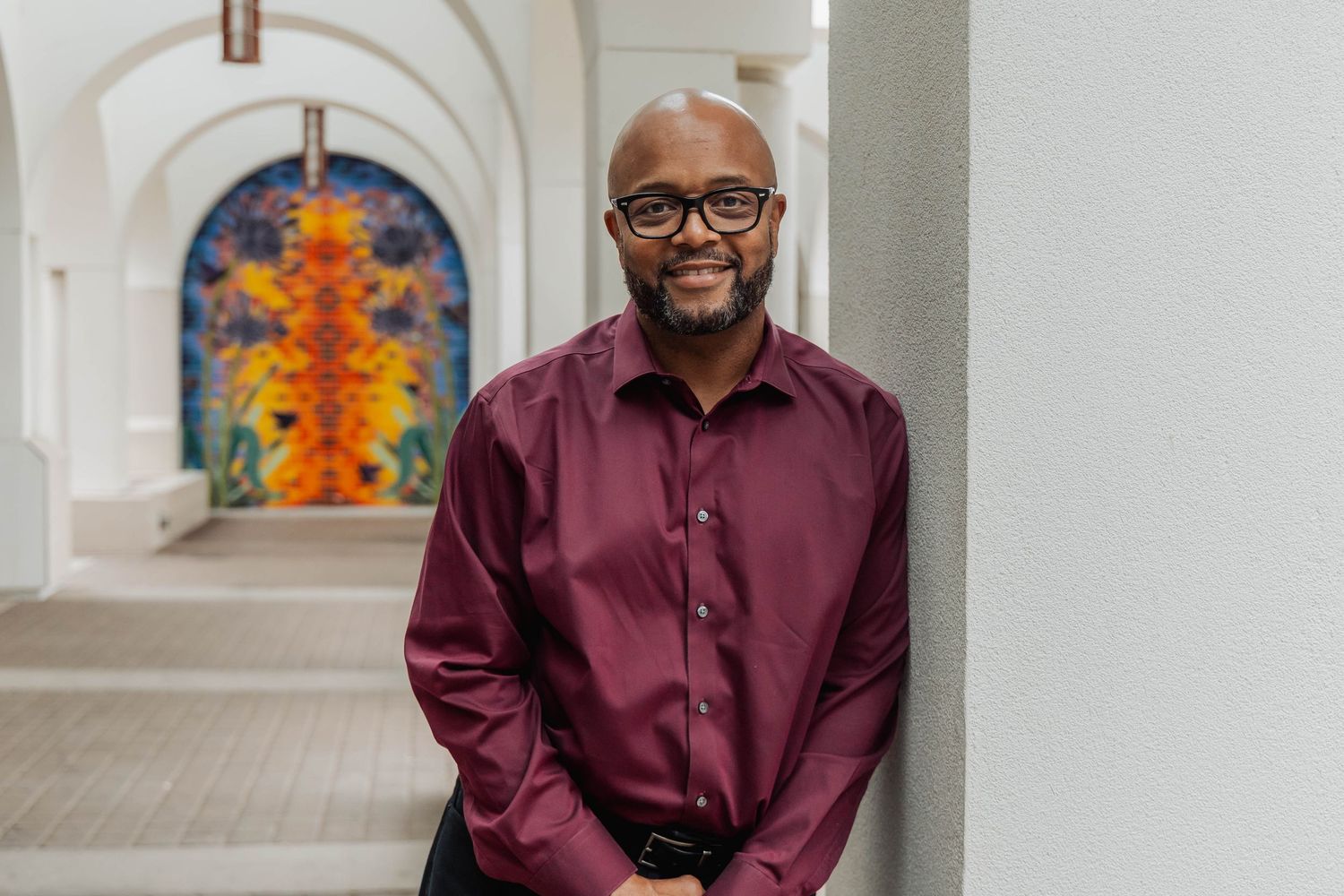 Professional wearing a burgundy button-down shirt smiling in an office setting.