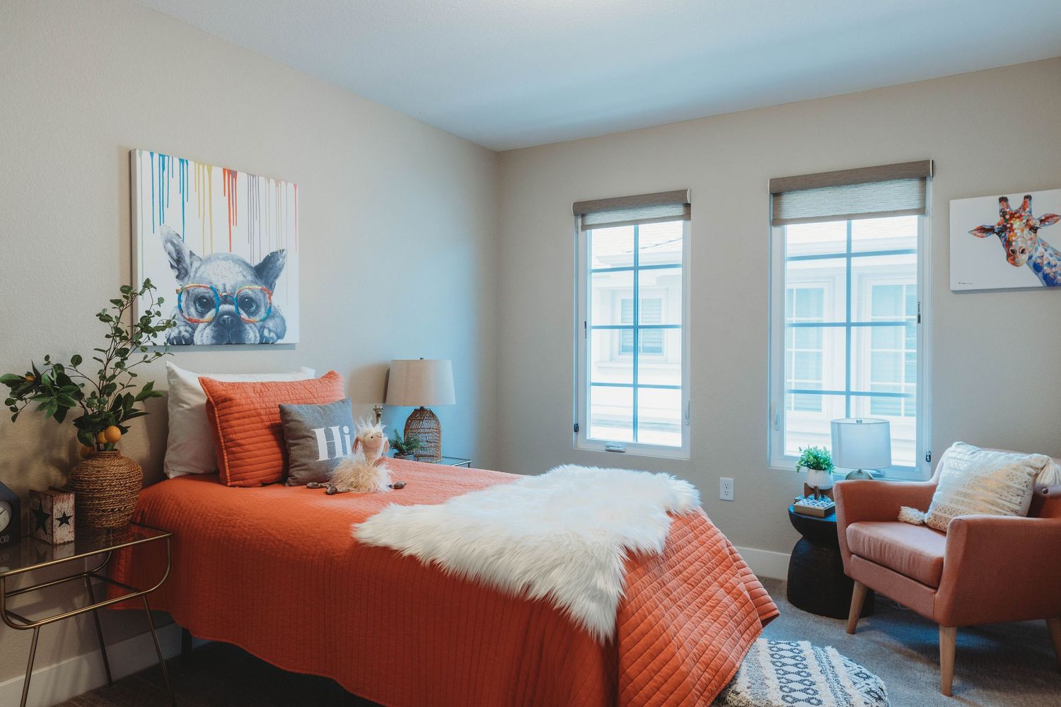 Stylish bedroom featuring coral bedding, blue artwork, and modern accent chair by windows.