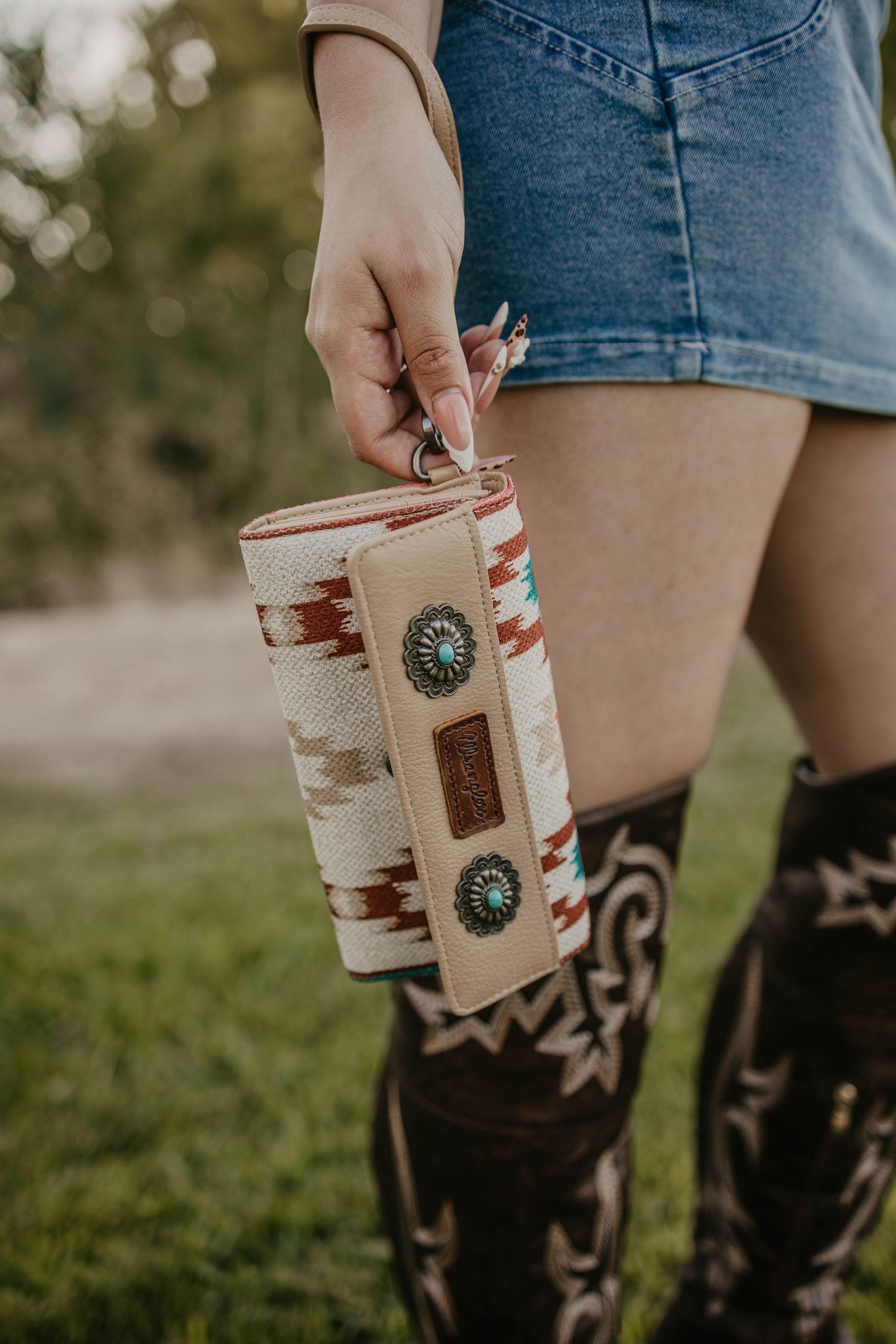 Decorative western style wallet with conchos shown with cowboy boots and denim shorts.