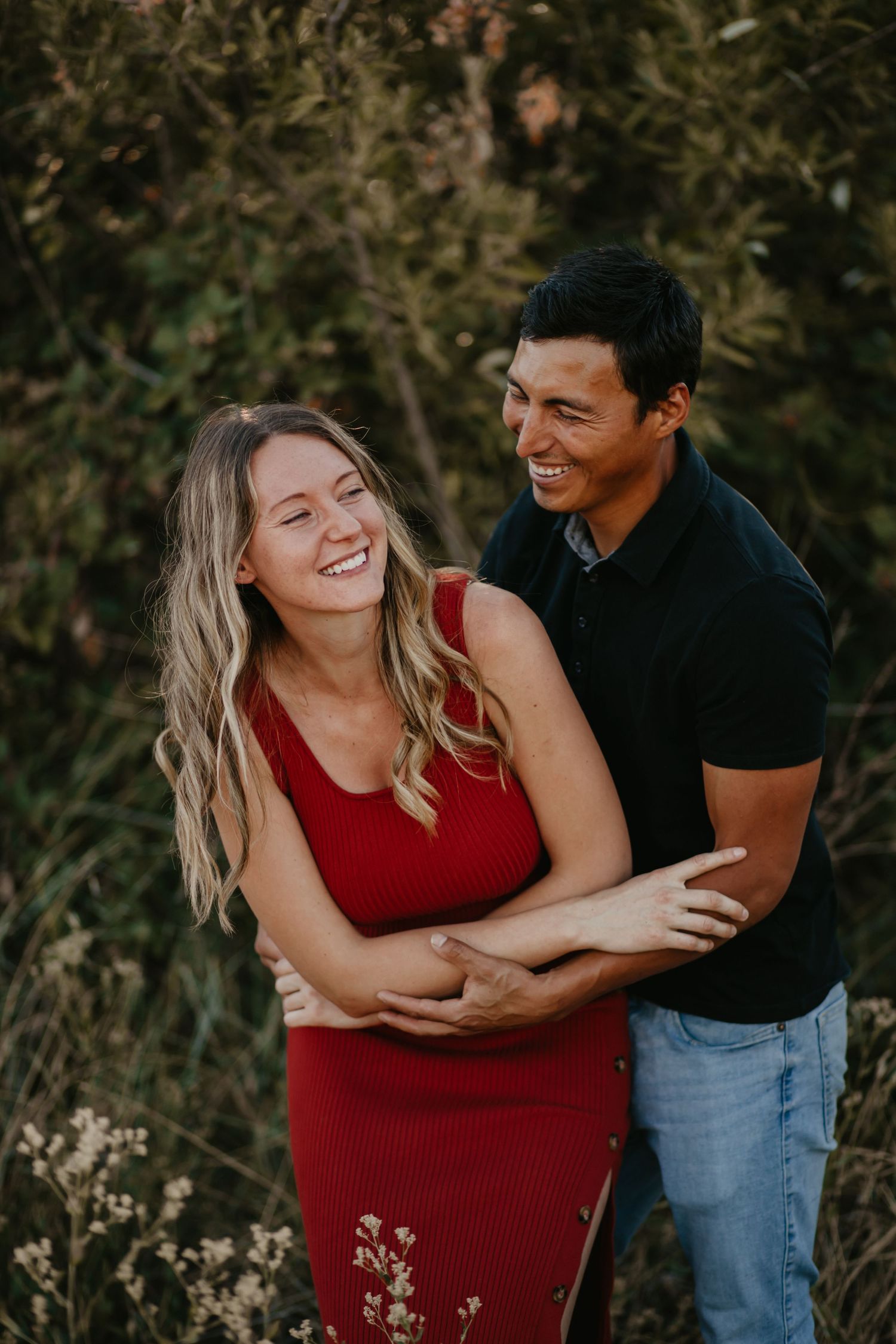 A couple laughs together during their outdoor photoshoot while wearing red and black casual attire.