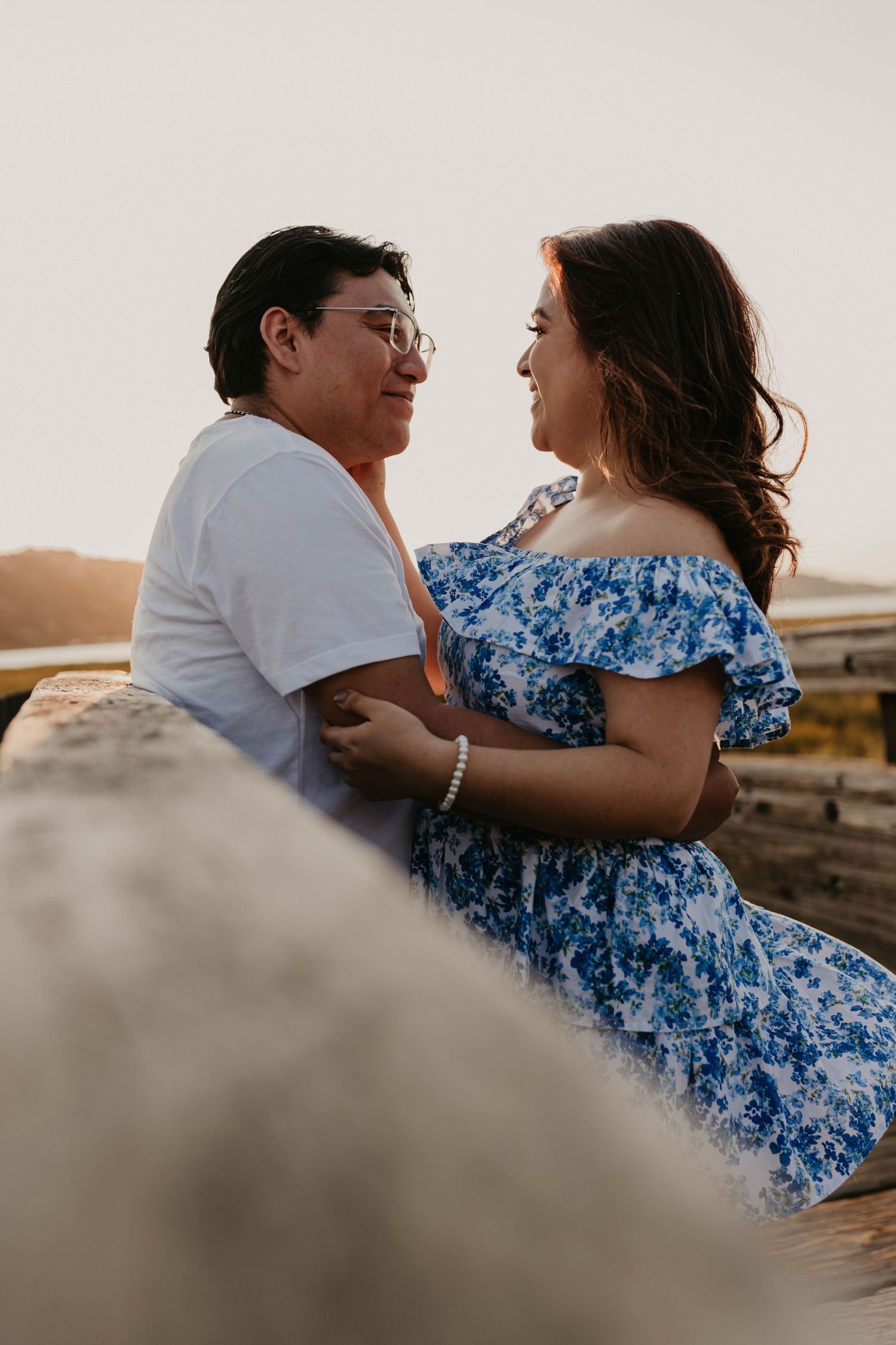 A couple sits close together on rocks during a romantic sunset photoshoot.
