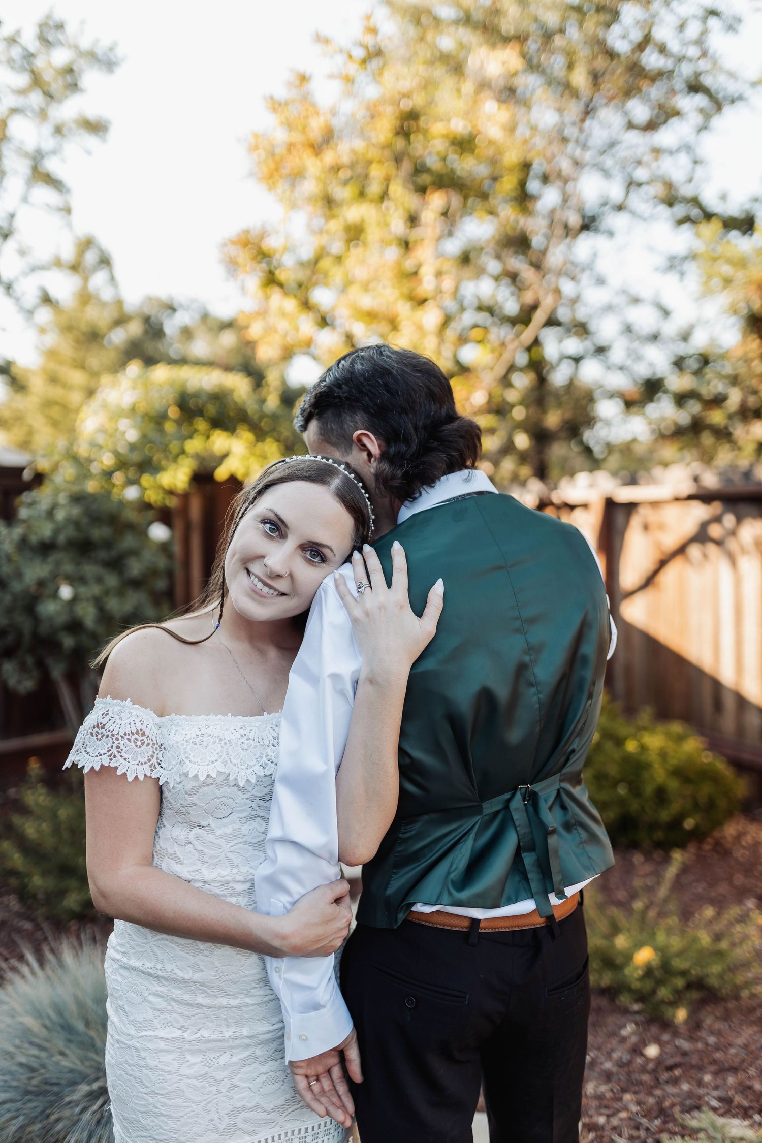 A bride in a white lace dress and groom in dark suit share joyful moments during their wedding photoshoot.