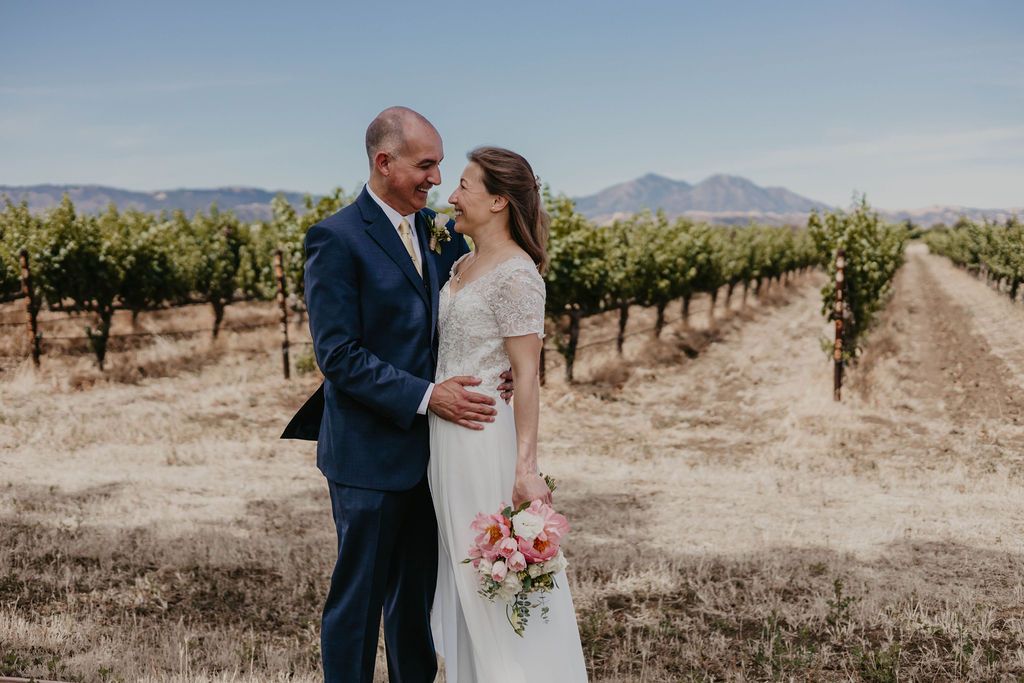 Elegant wedding portrait in vineyard with rolling hills and mountains in background.