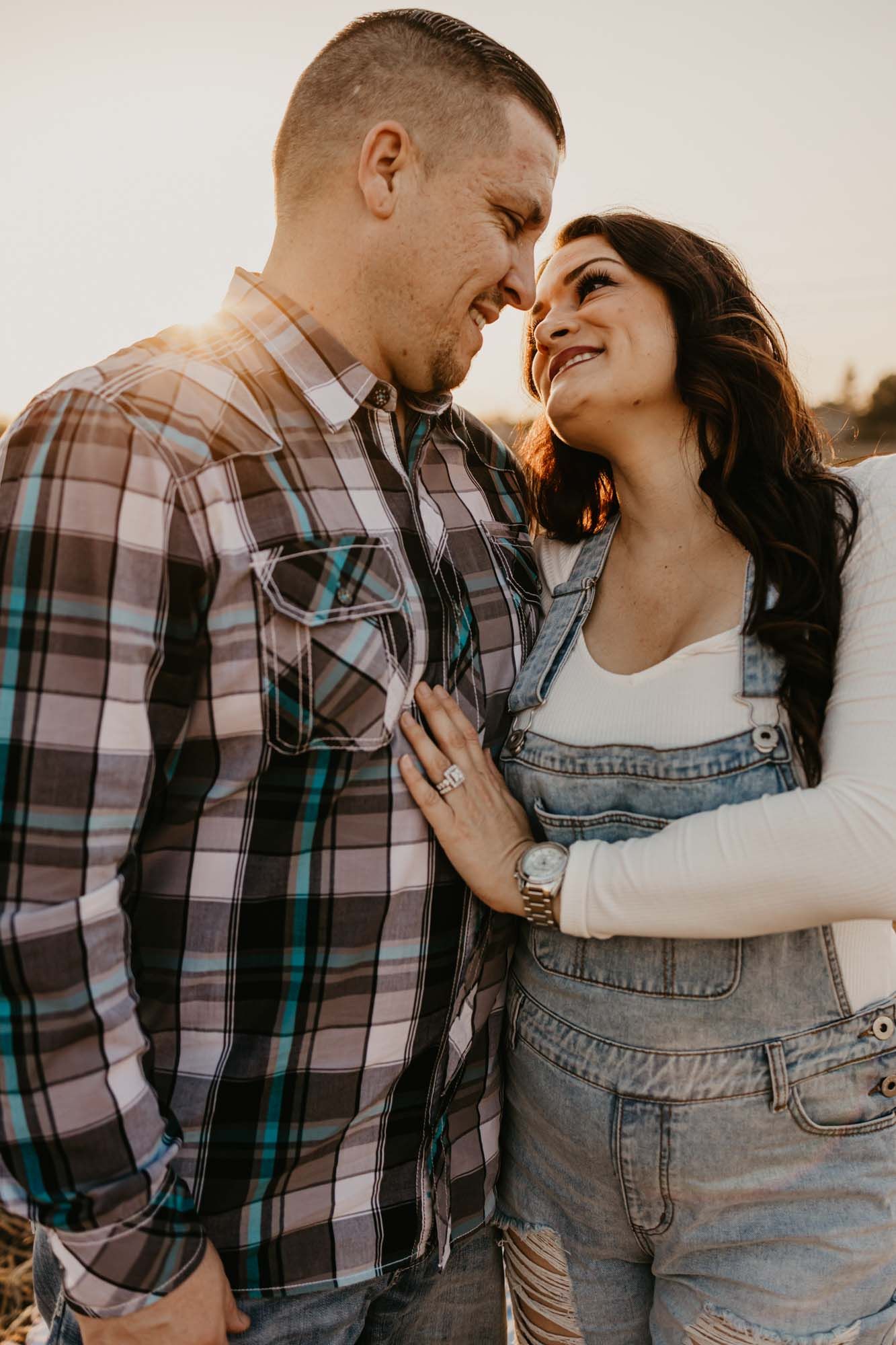 Intimate moment between couple in plaid shirt and denim overalls during sunset photoshoot.