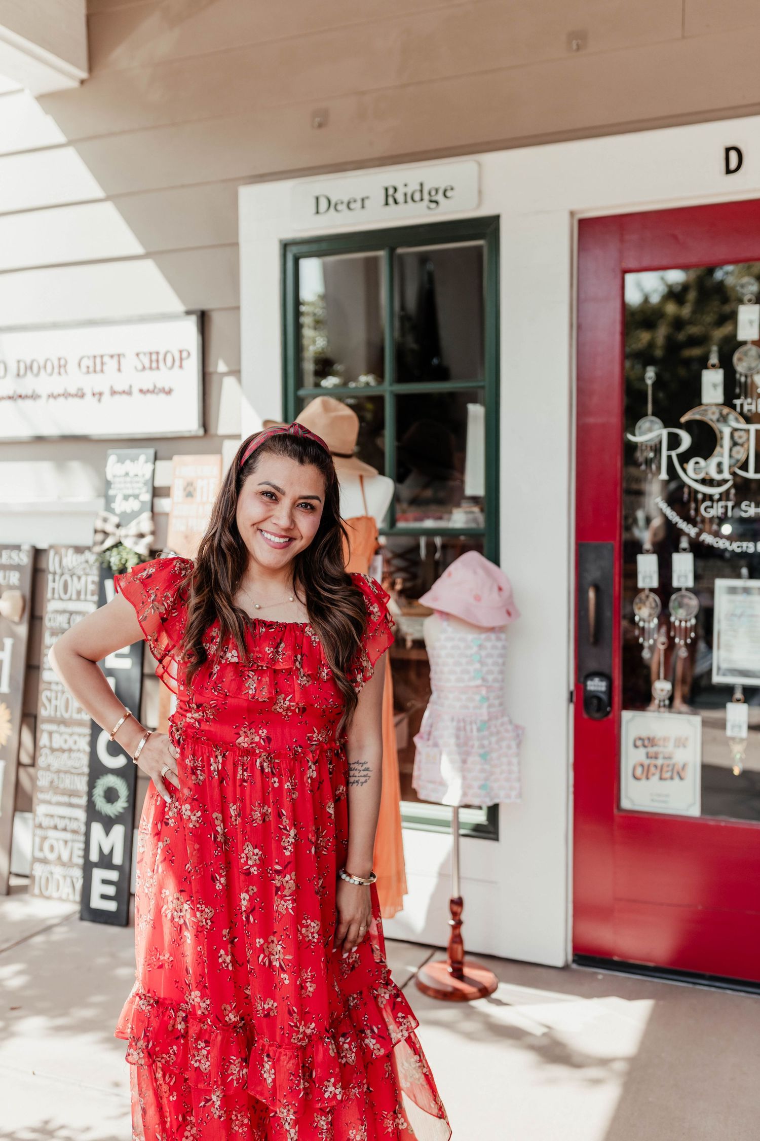 A bright red floral maxi dress worn outside The Red Door Gift Shop storefront on a sunny day.