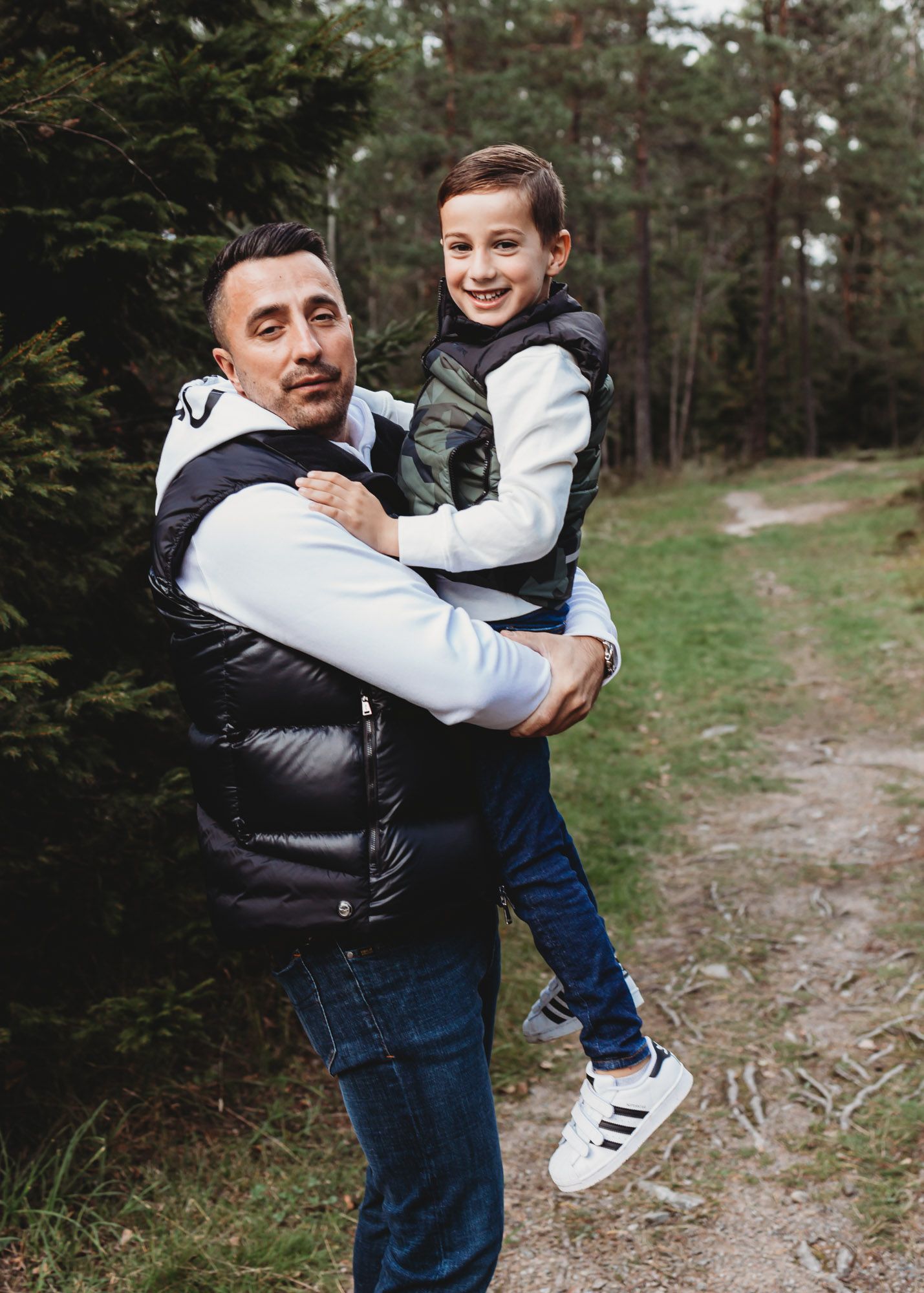 Joyful moment shared between adult and child on hiking trail wearing matching black vests.