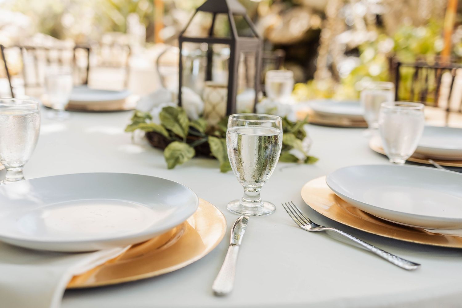 Elegant table settings with gold charger plates and white linens for a formal wedding reception.