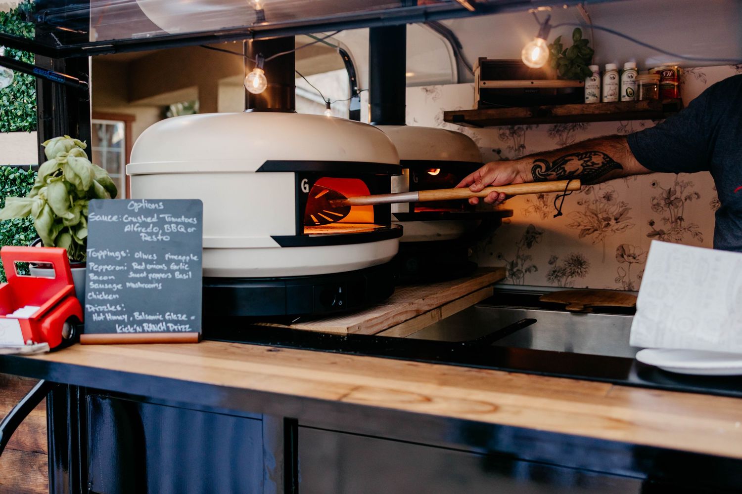 Pizza being prepared in a rustic kitchen with wooden surfaces and dark countertops.