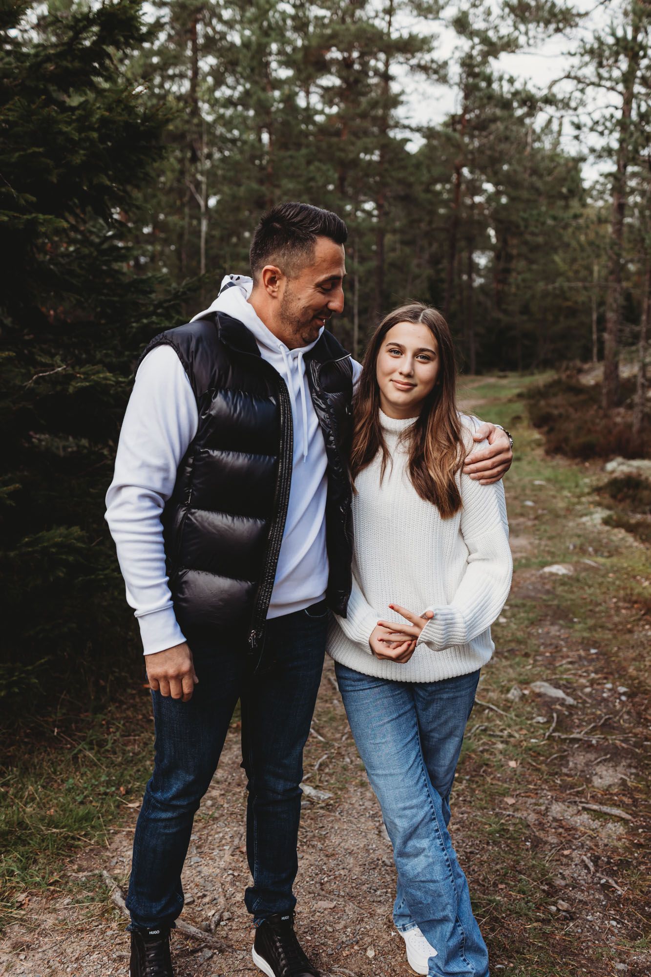 Couple in casual attire standing together on a forest path during autumn.