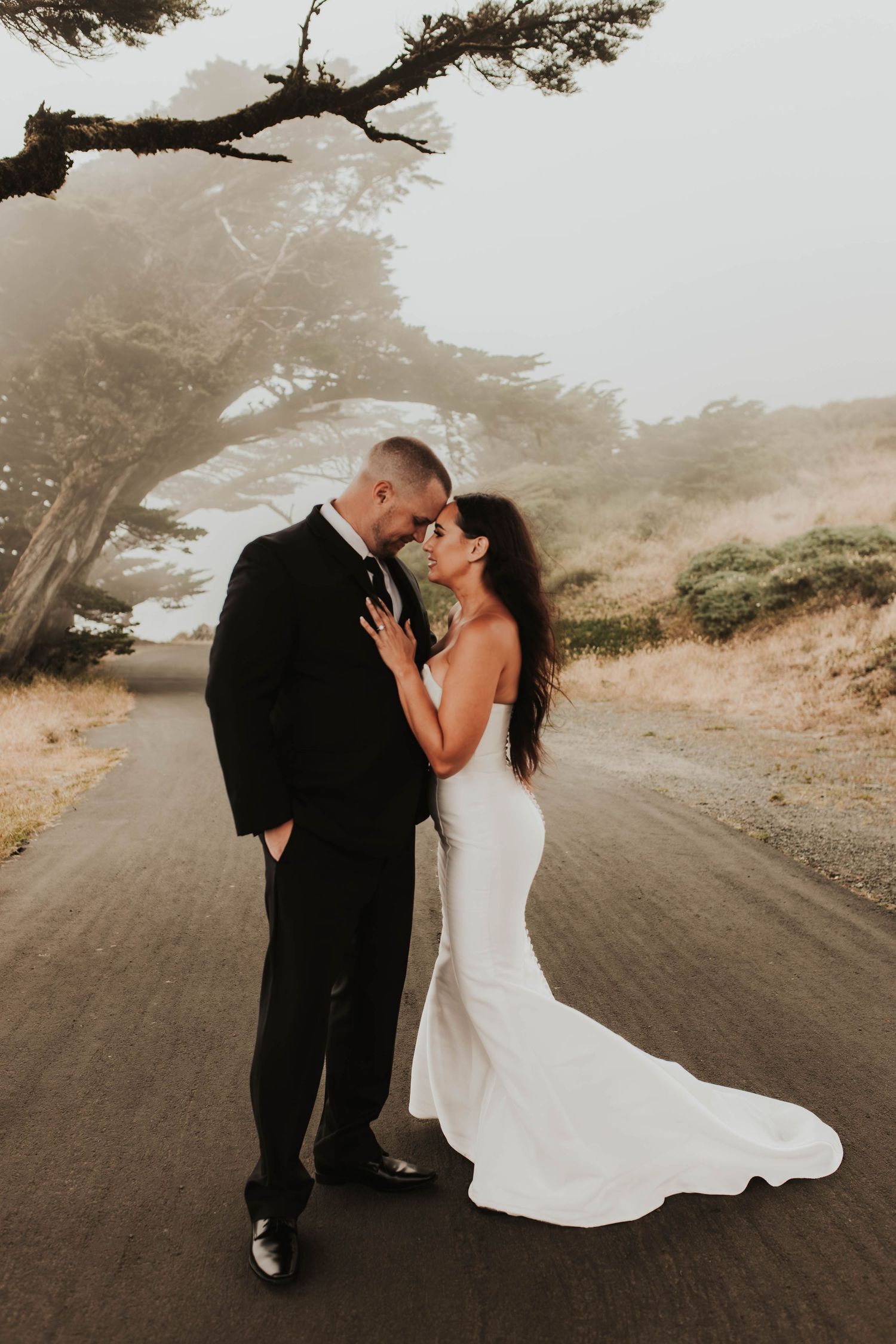 A romantic wedding portrait under cypress trees on a foggy dirt road.