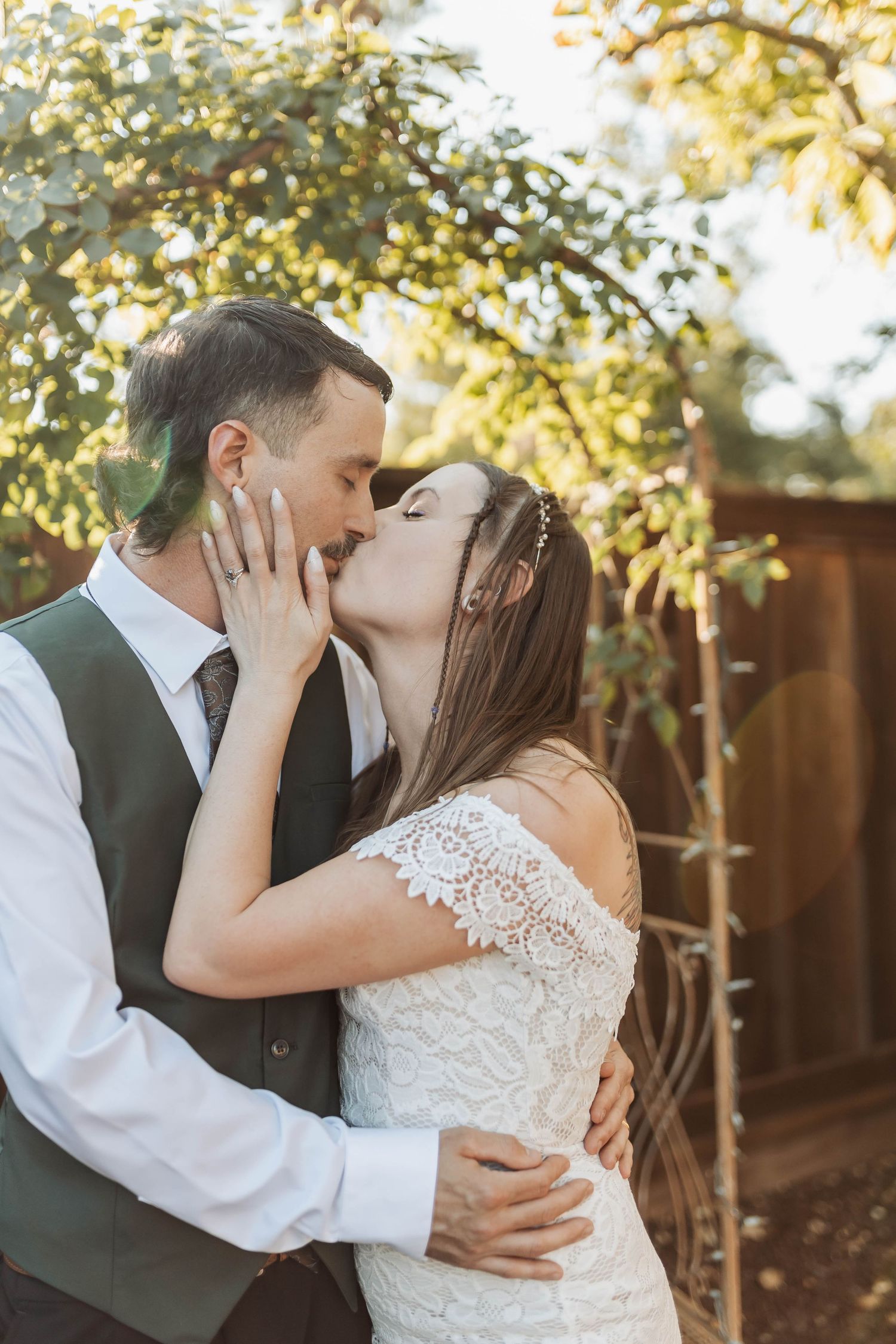 Romantic kiss between newlyweds in garden setting with golden sunlight.