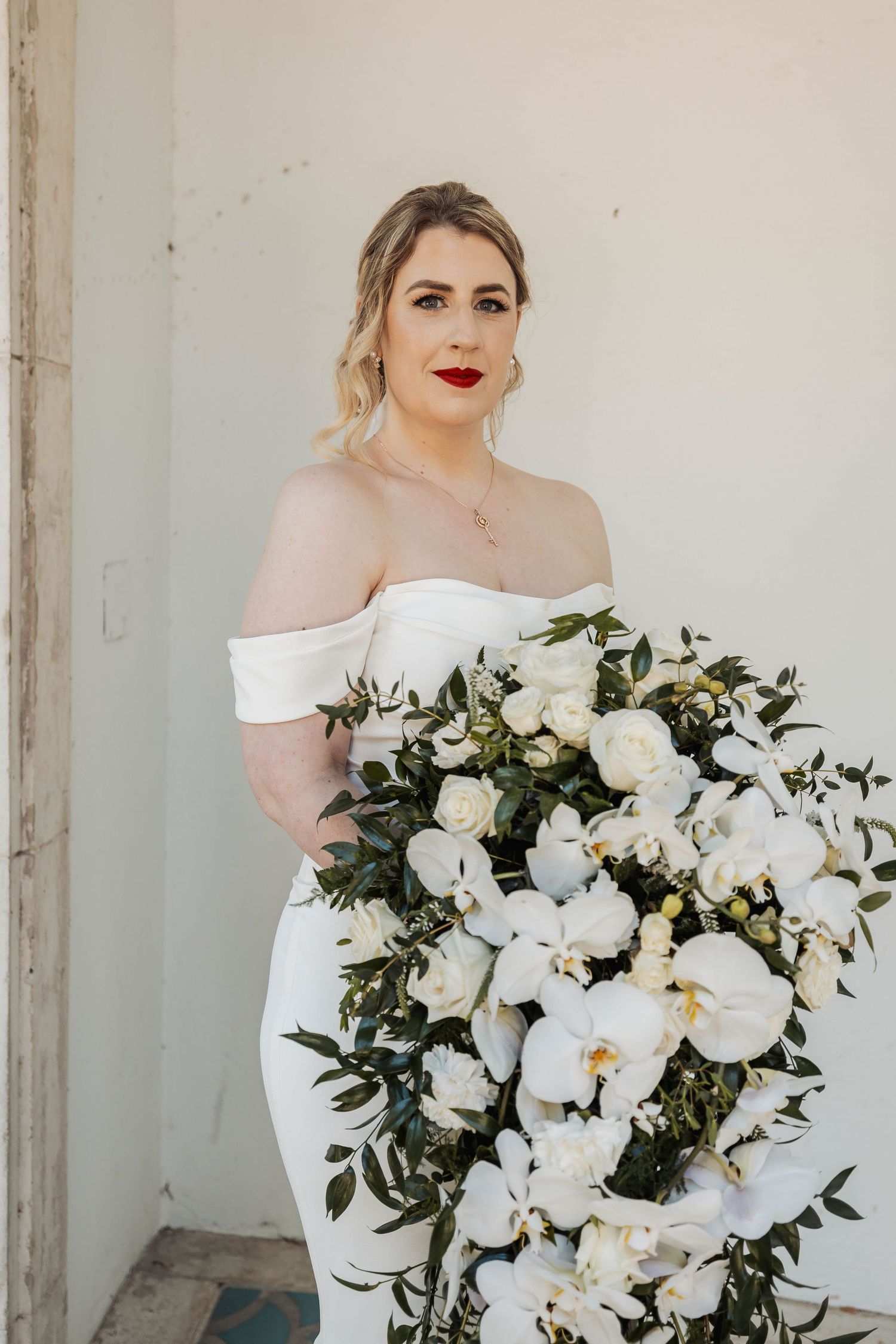 An elegant white floral bouquet with orchids and greenery against a light backdrop.