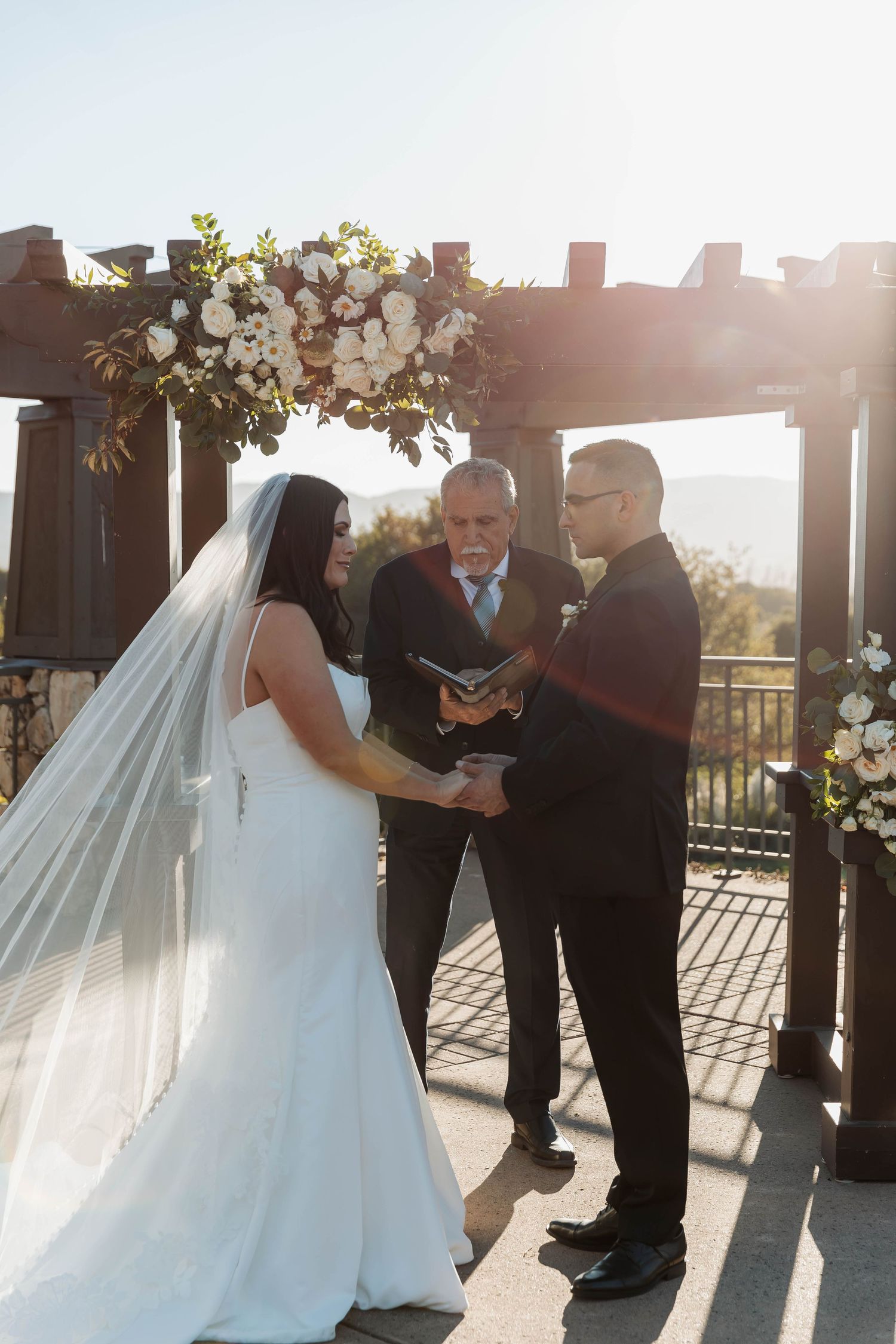 Outdoor wedding ceremony under a decorated pergola during golden hour.