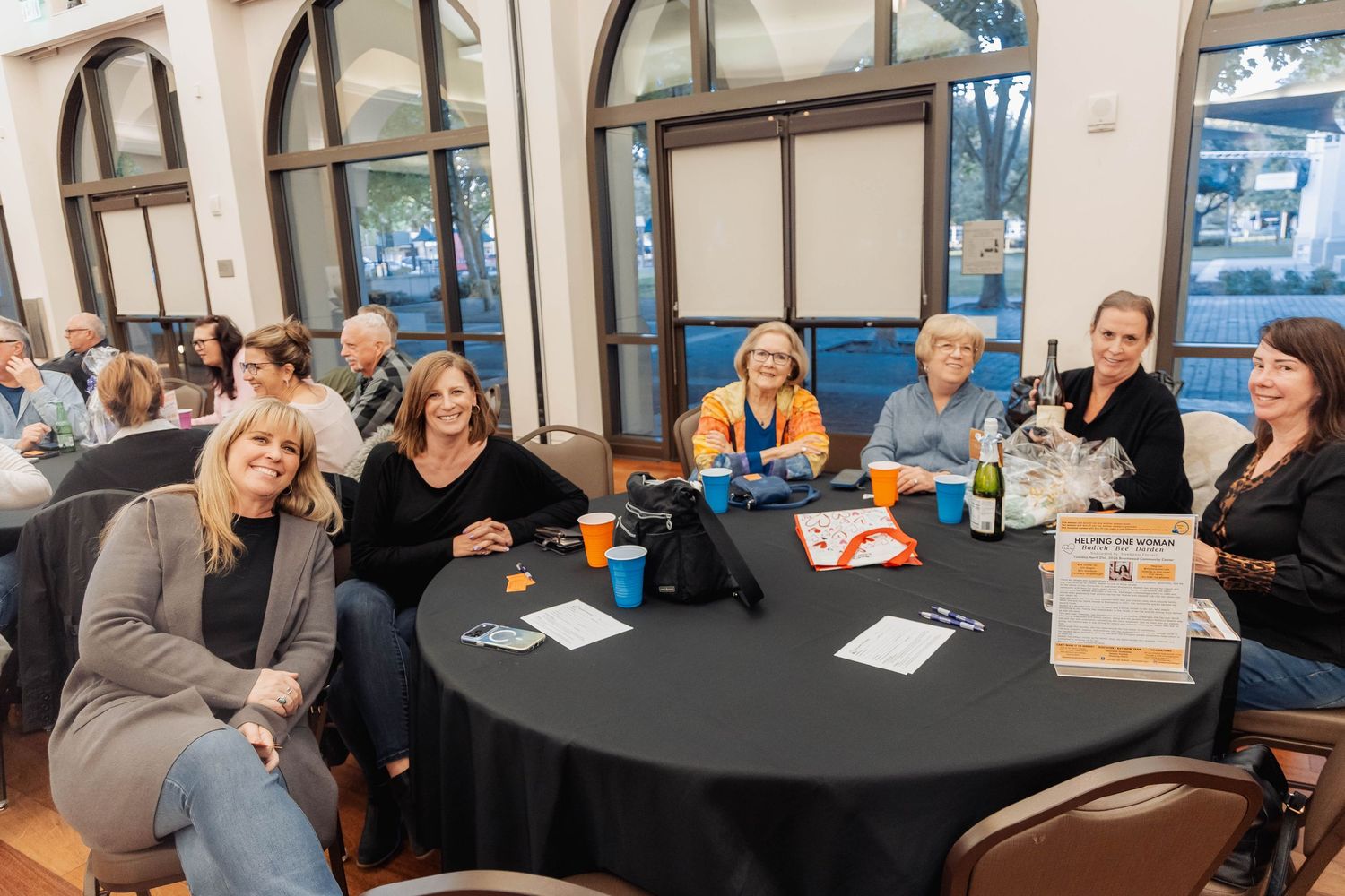 Group of women smiling at a round table with black tablecloth at an indoor social event or networking gathering.