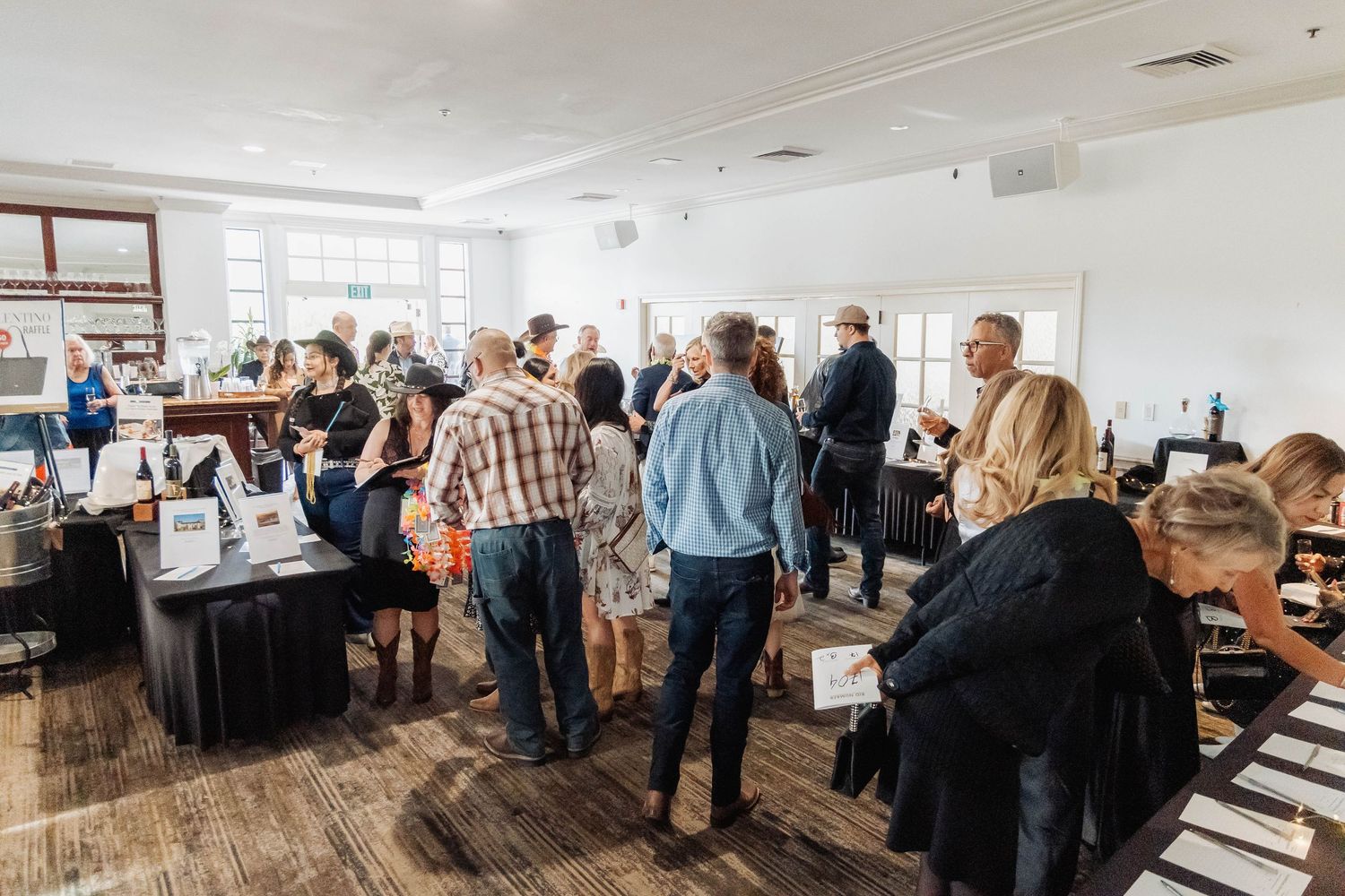 Guests mingle at an indoor wine tasting event in a bright, modern venue with large windows.