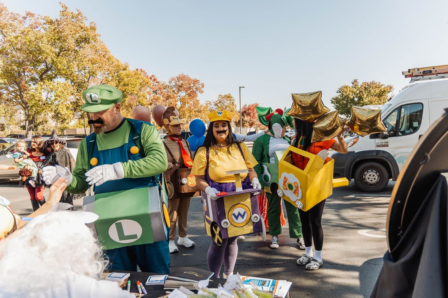 Group of attendees in colorful costumes gathering in a parking lot during a daytime event.
