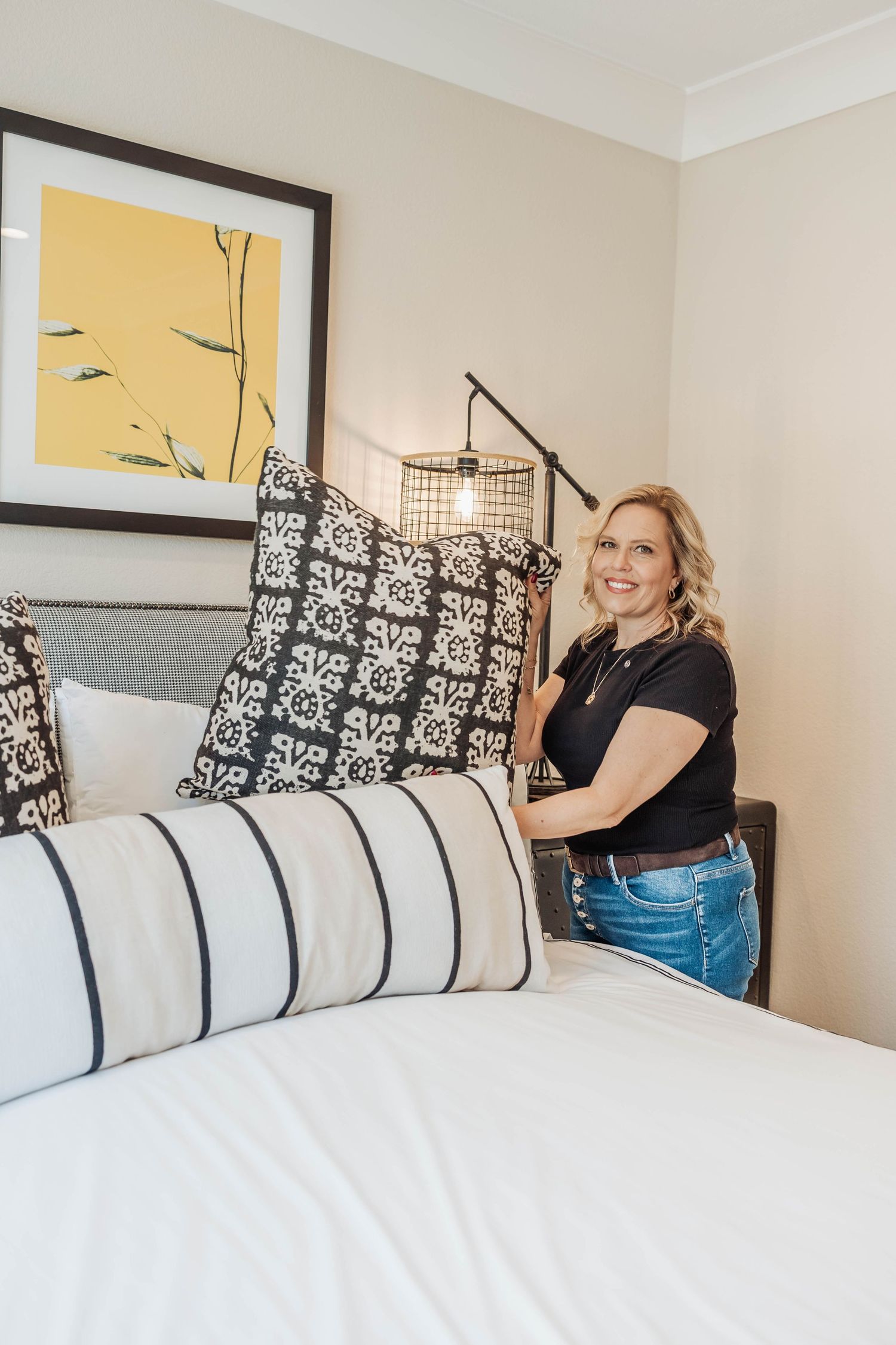 Modern bedroom decor with black and white pillows and yellow artwork on wall.