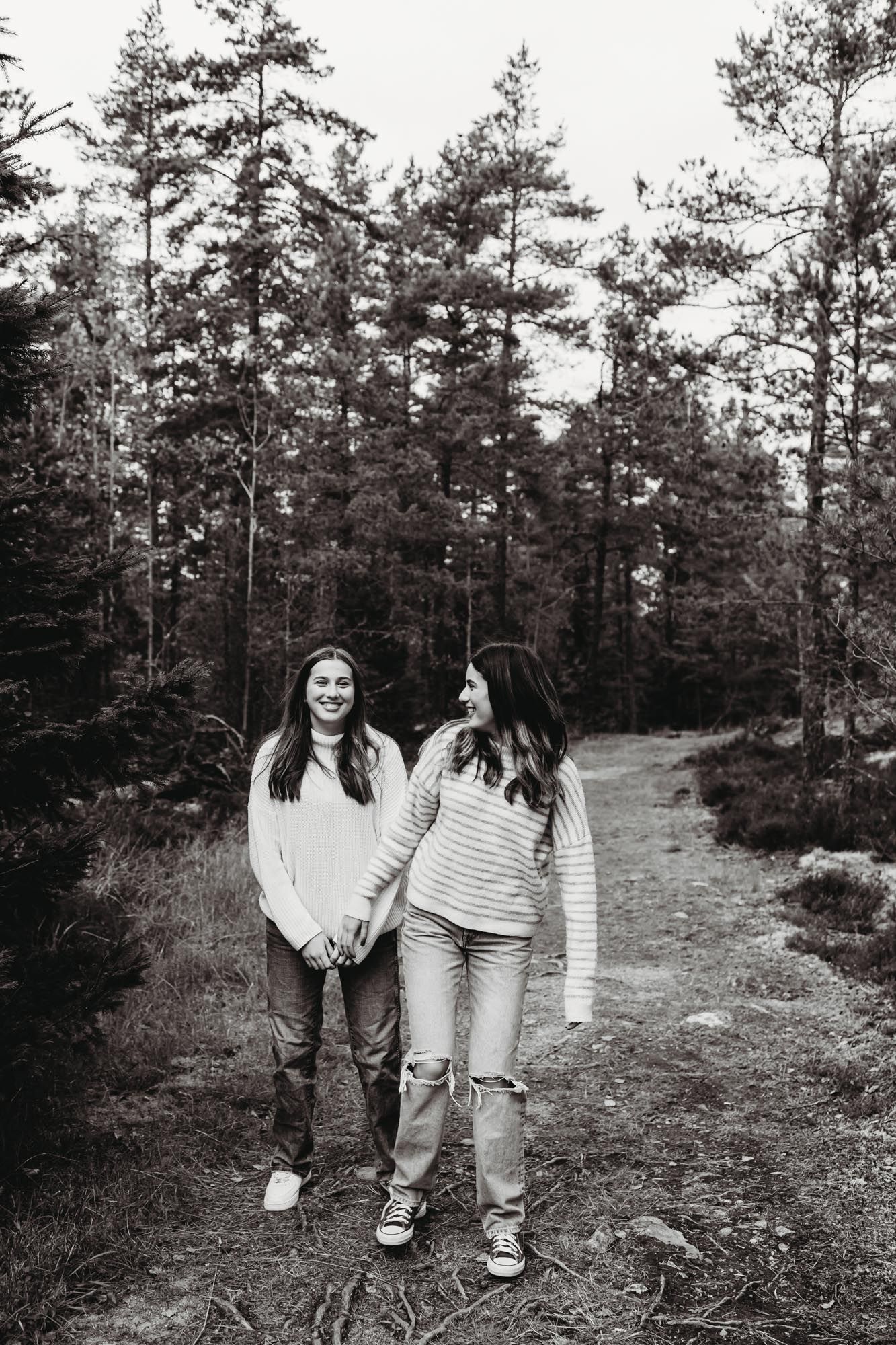 Two people in casual winter attire sharing a laugh while walking on a wooded trail.