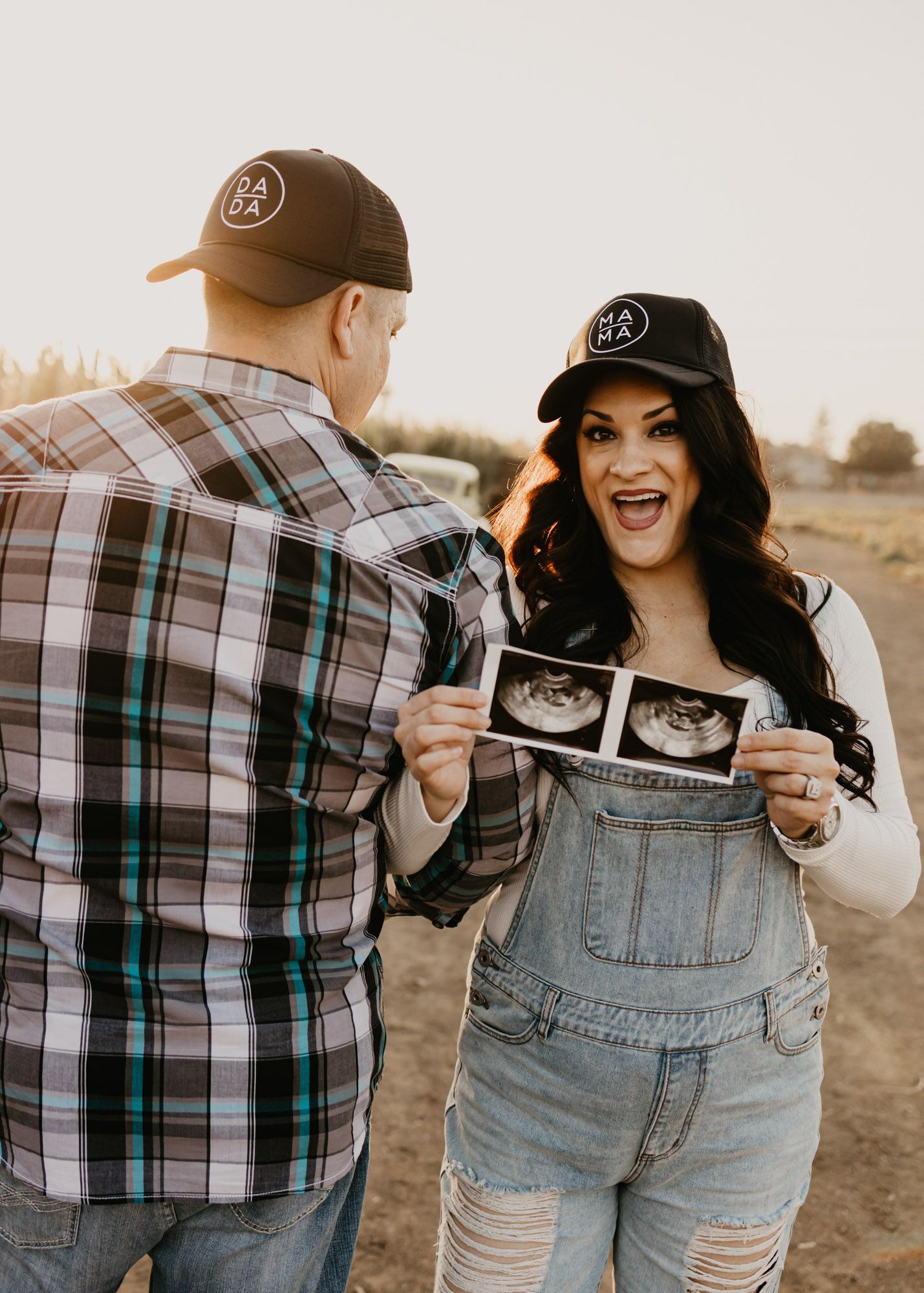 Couple sharing joyful pregnancy announcement with ultrasound photos in outdoor setting.