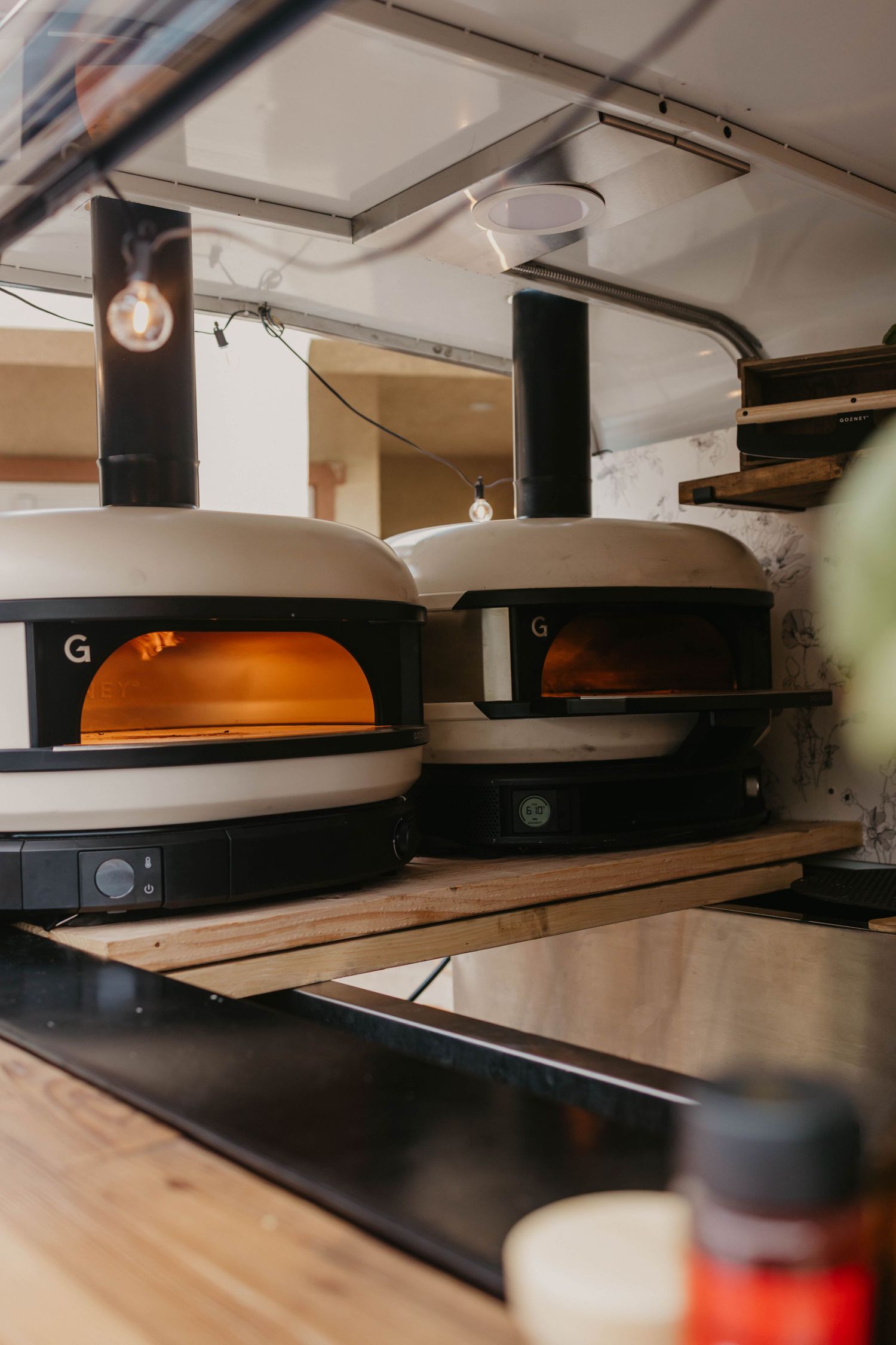Row of industrial pizza ovens glowing orange in a professional kitchen setting.