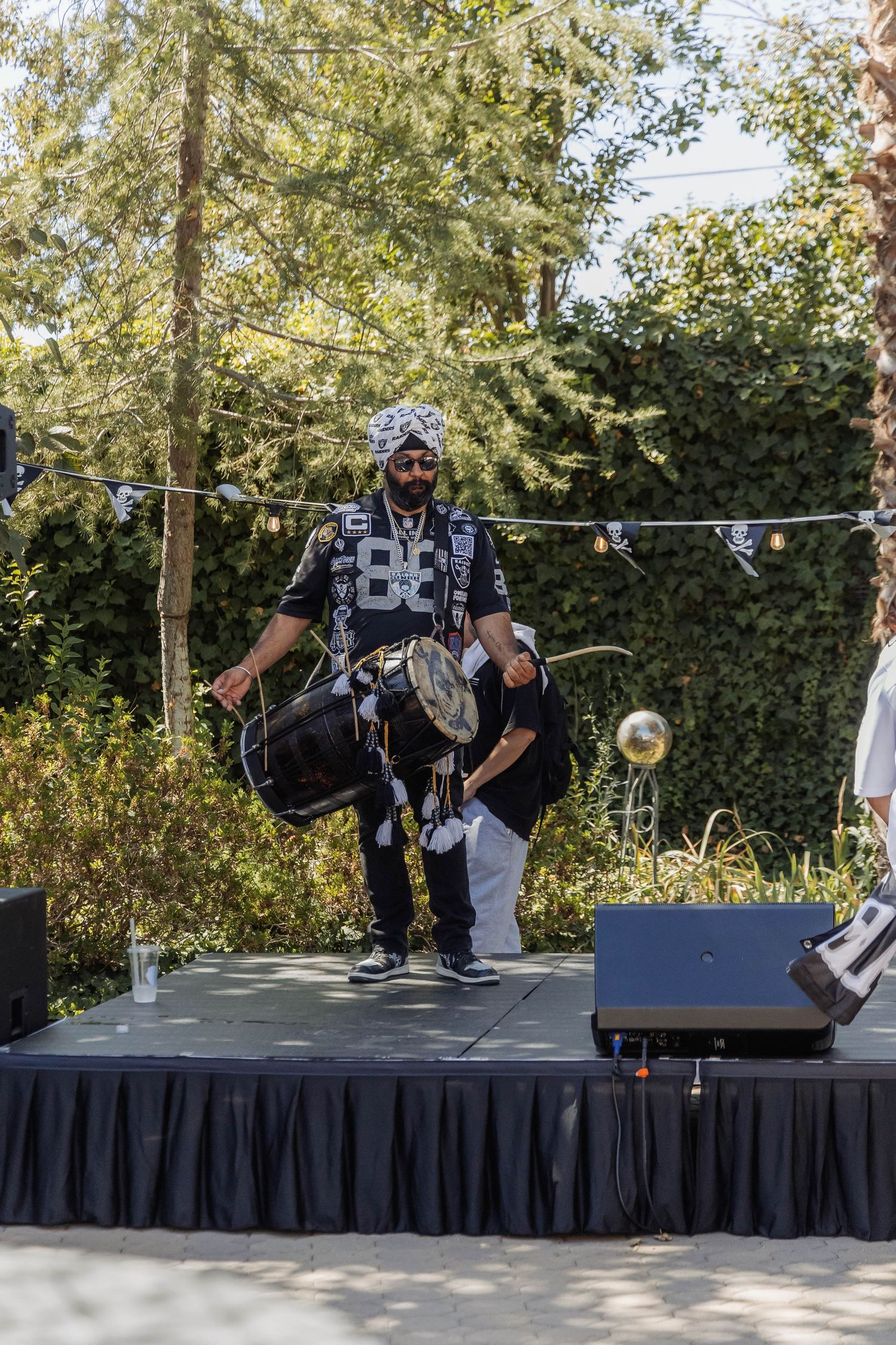 Musician performs on outdoor stage wearing Raiders gear while playing drums at a fan event.