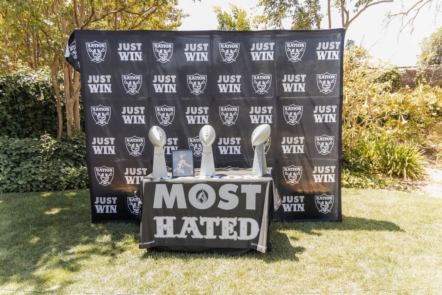 Raiders NFL backdrop with Vince Lombardi trophies and a Most Hated themed table display outdoors.