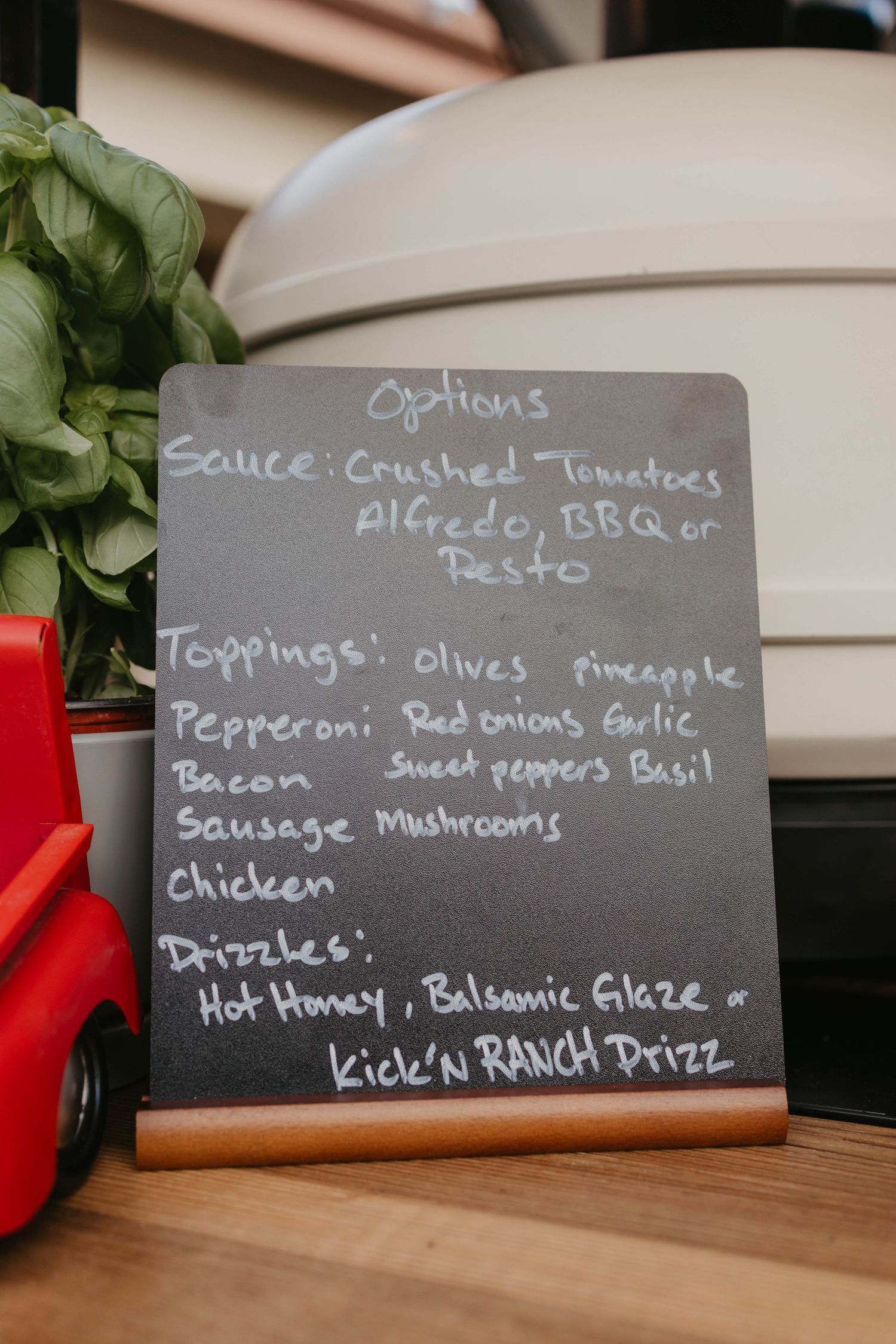 Chalkboard menu displaying pizza toppings, sauces and options at a restaurant.