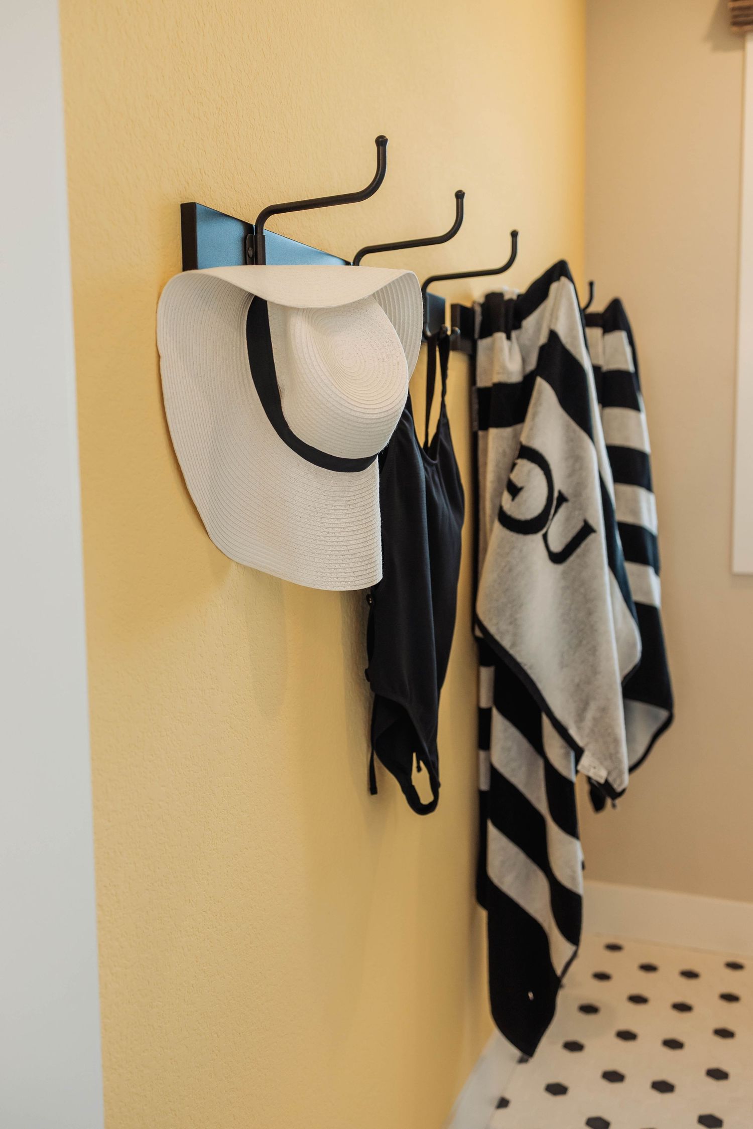 Bathroom wall with black hooks displaying black and white patterned towels against beige walls.