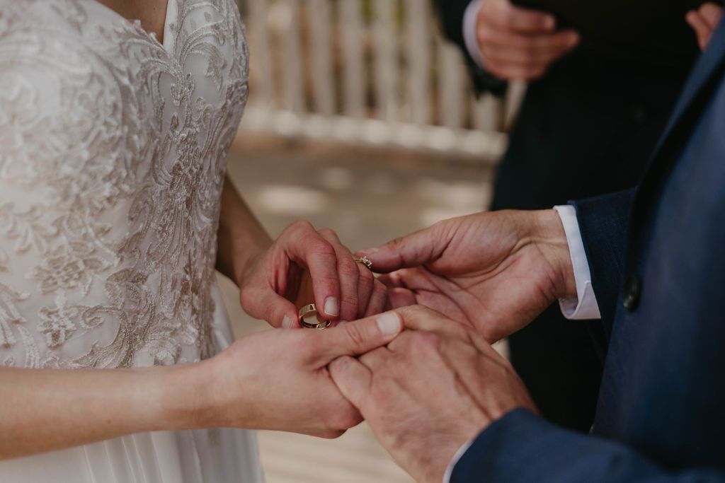 Close-up shot of wedding ring exchange between couple in formal attire.