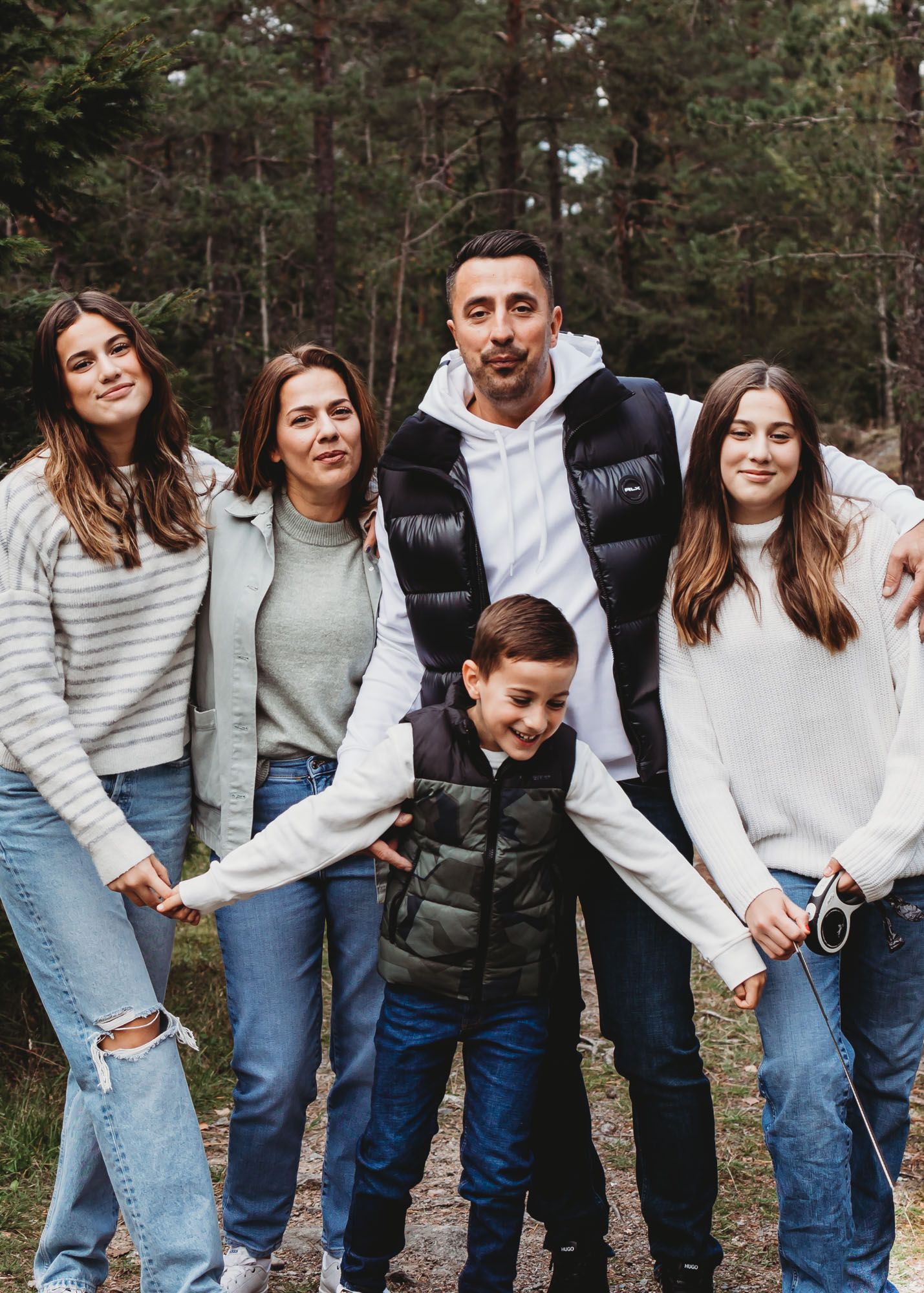 A family group photo in casual wear standing together on a forest path.