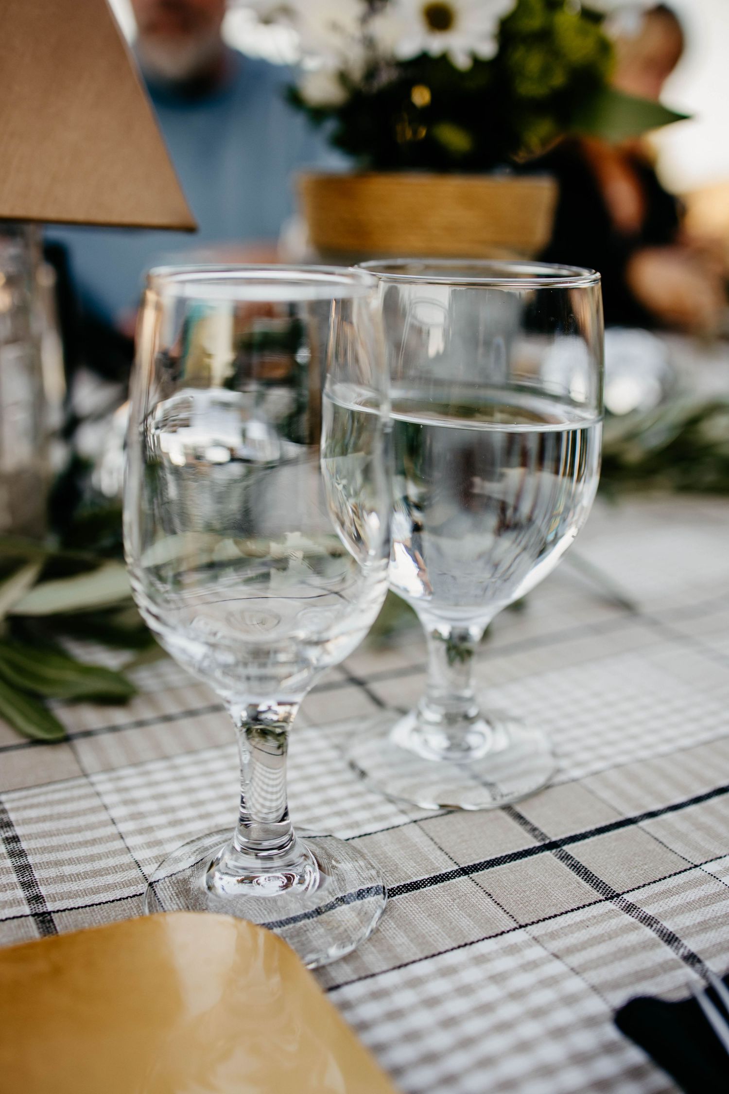 Wine glasses set on a checkered tablecloth for an outdoor dining event.