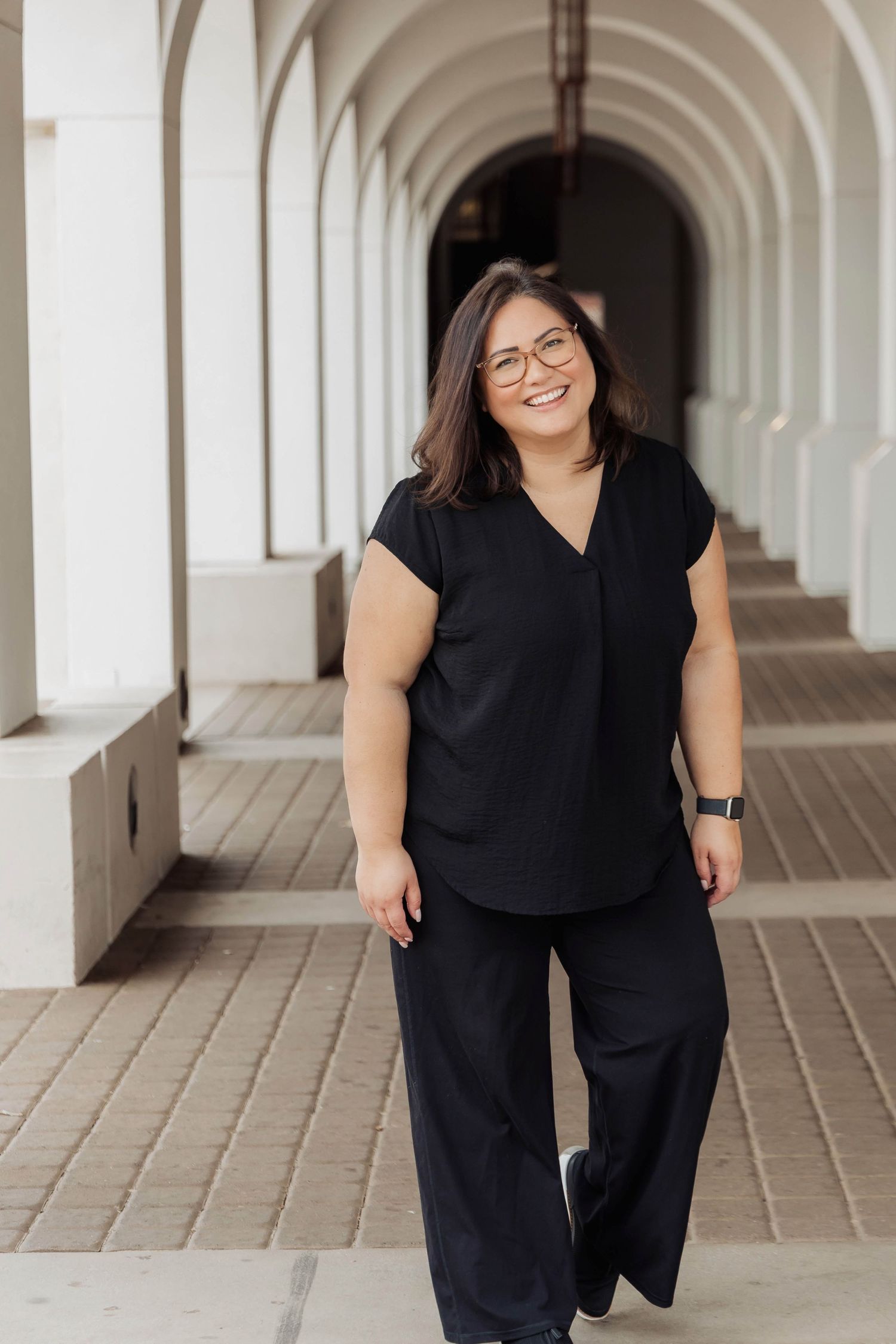 A figure in black attire poses playfully in a series of shots along a white arched colonnade hallway.