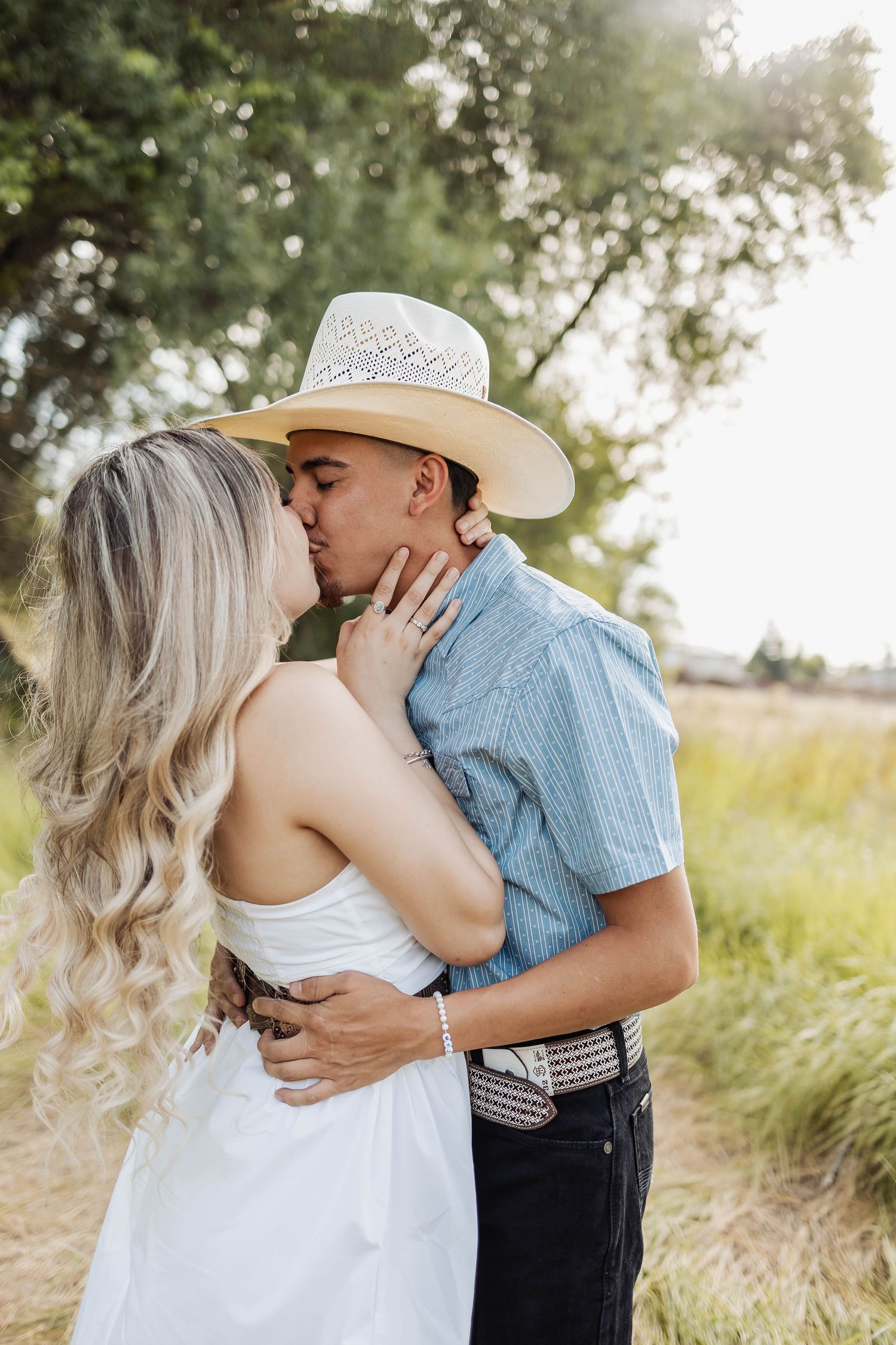 Romantic couple in western style clothing sharing kiss in sunlit field.