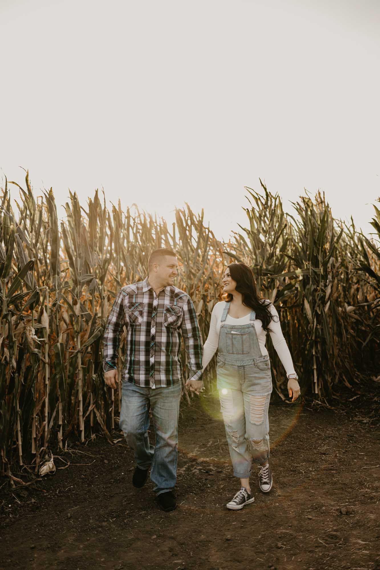Two people walking together on a dirt path surrounded by tall dried corn stalks.