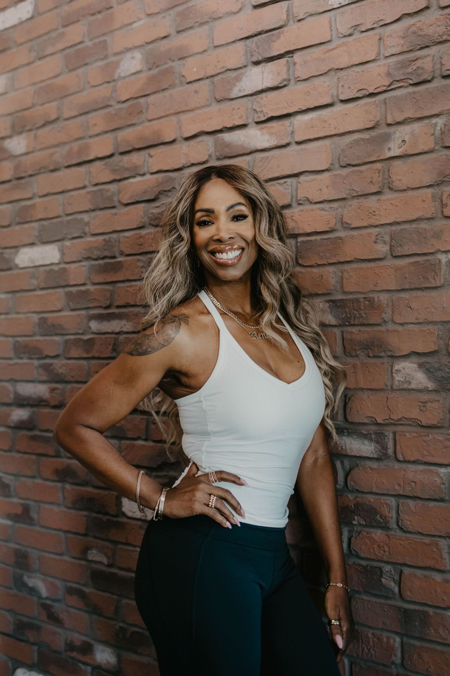 Professional portrait session against brick wall featuring casual white tank top and dark pants.