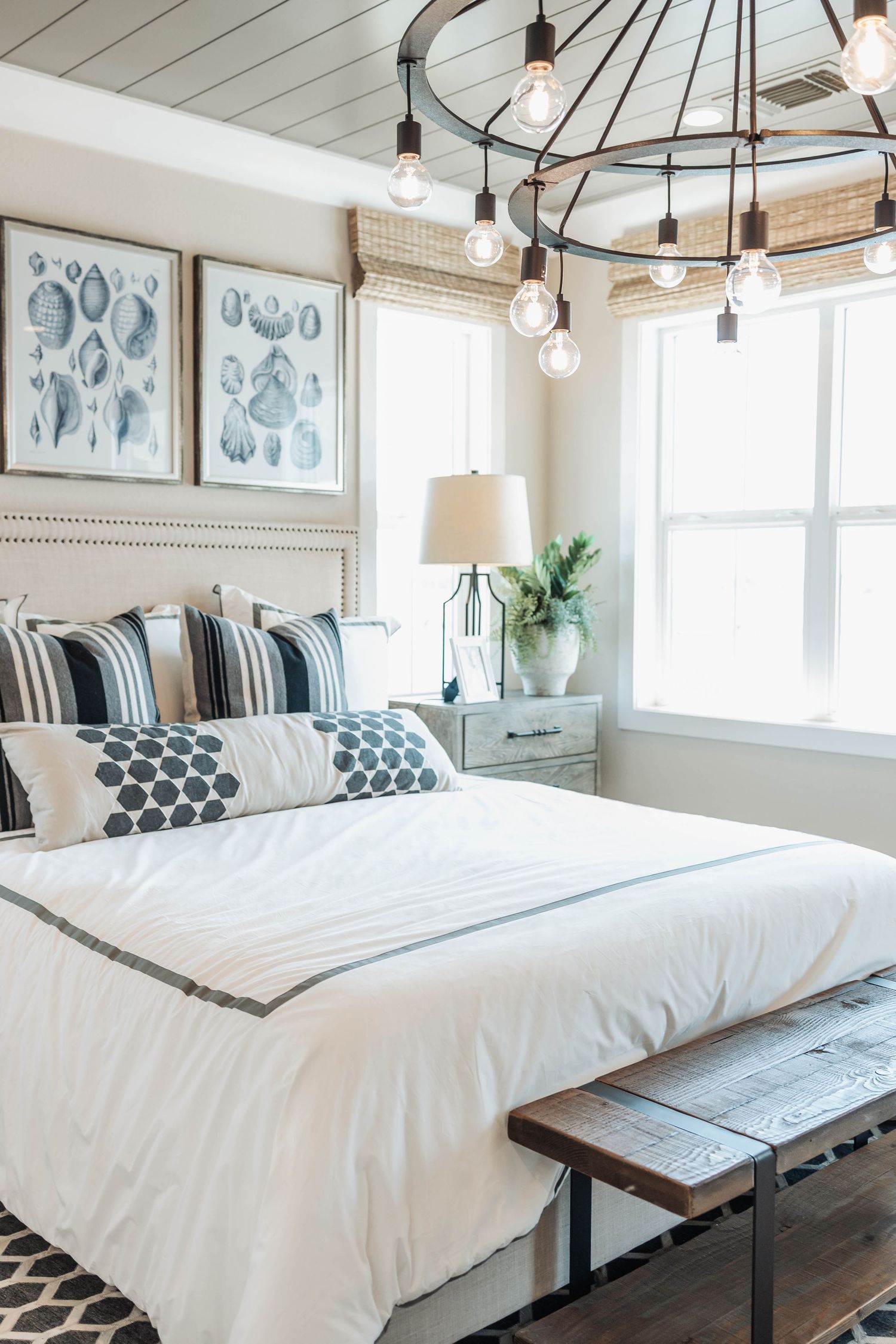 Coastal style bedroom with string lights, white bedding, and blue nautical artwork above the headboard.