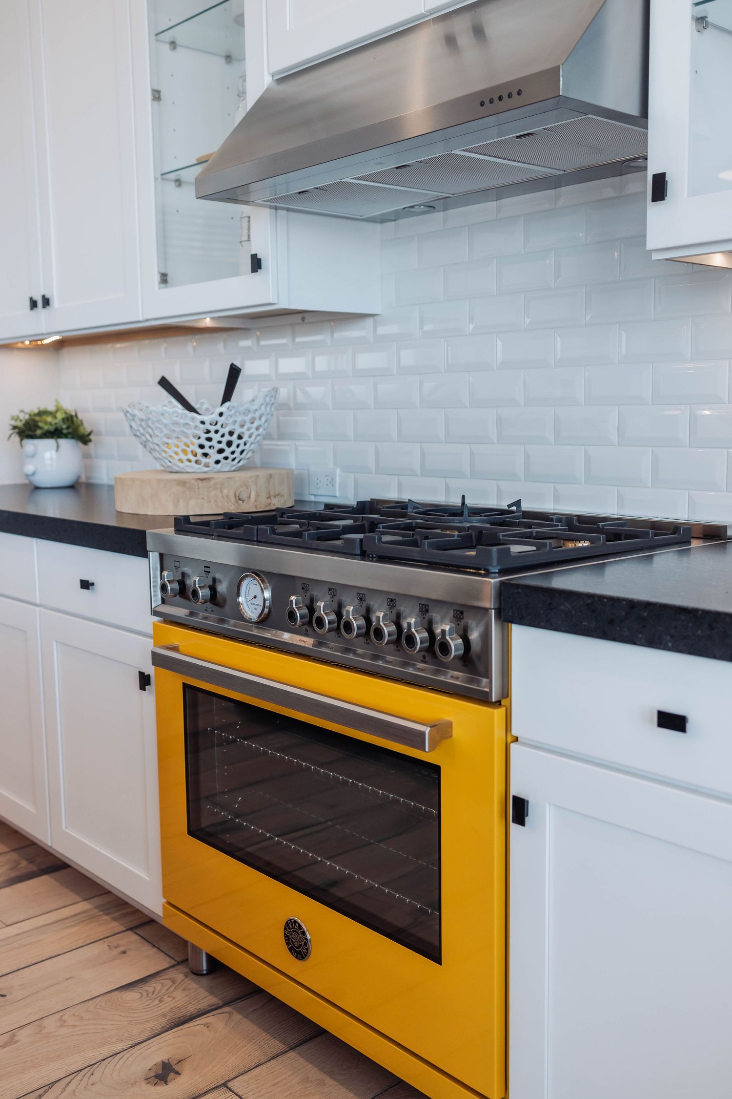 Yellow professional gas range with multiple burners set against white cabinetry and tile backsplash.