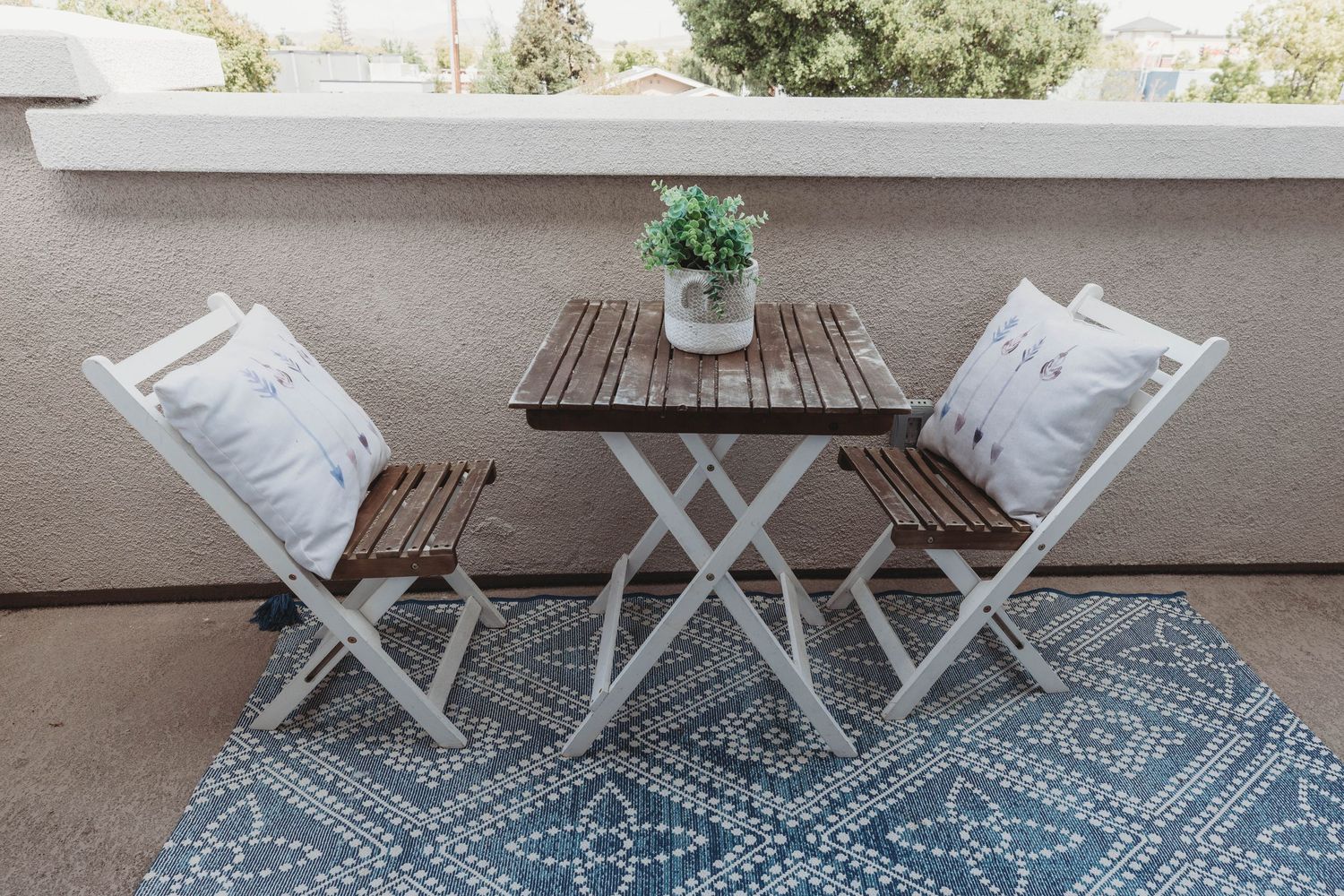 Cozy balcony setup with folding wooden furniture and blue geometric outdoor rug.