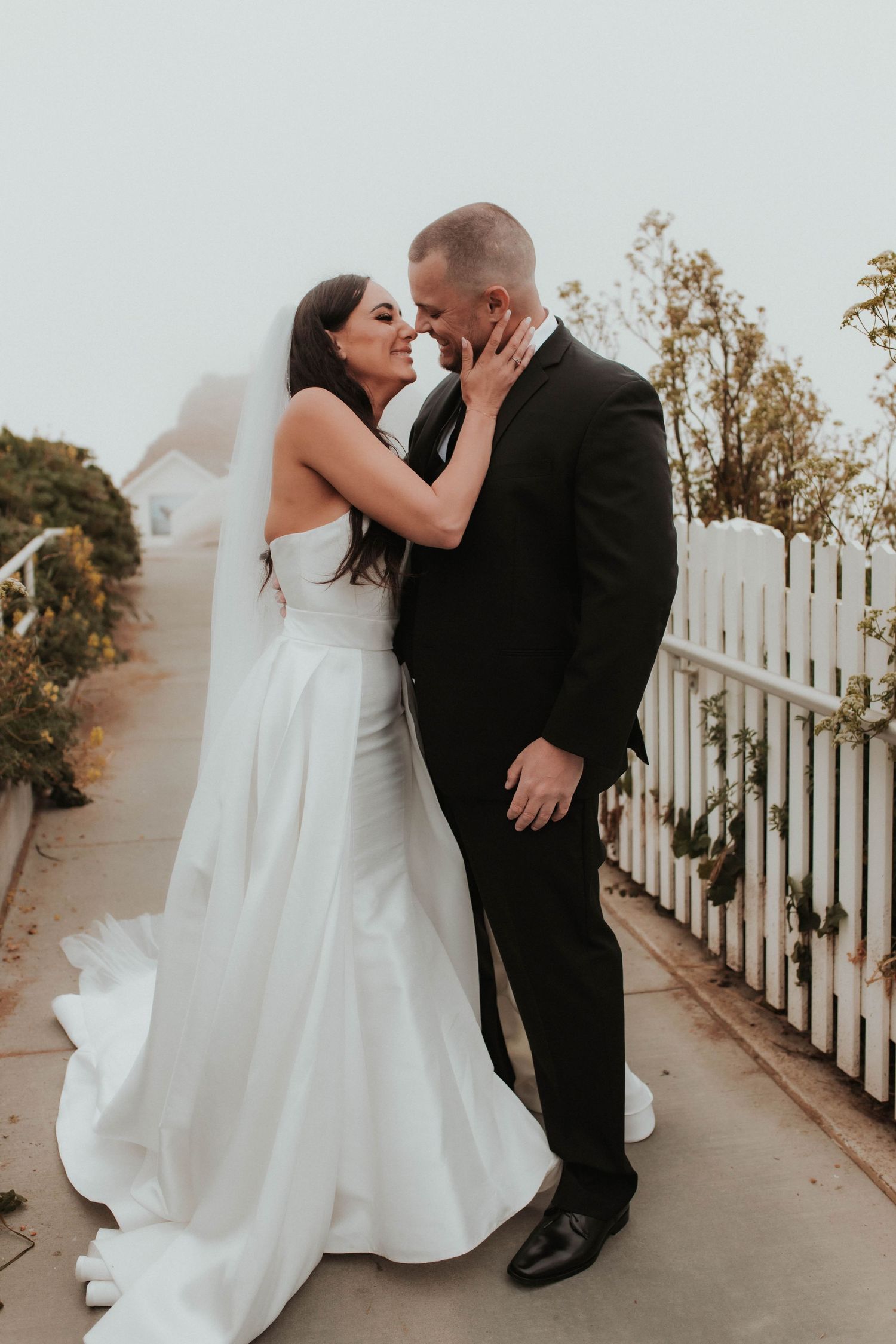 Intimate moment between wedding couple on pathway surrounded by garden foliage.