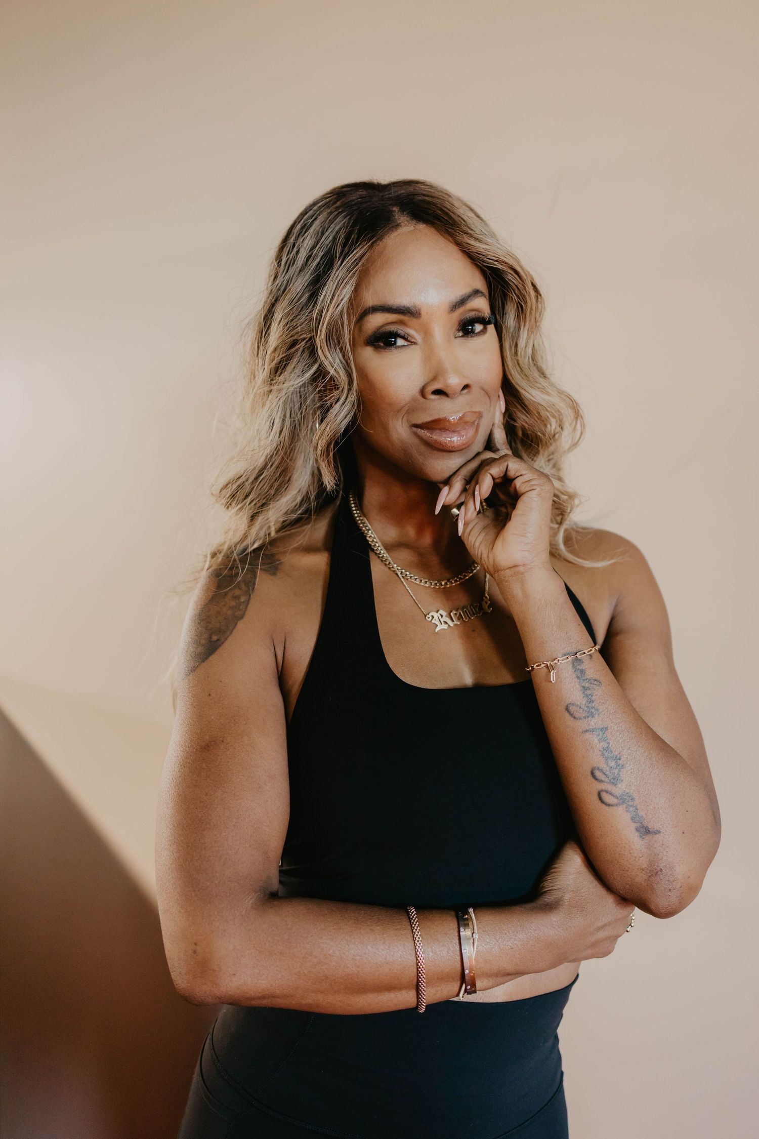 Athletic woman in black tank top poses confidently against beige background.