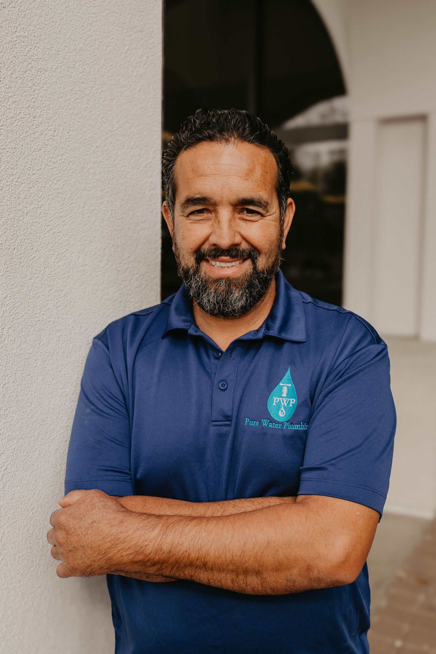 Staff member in blue polo shirt with company logo posing against white wall.