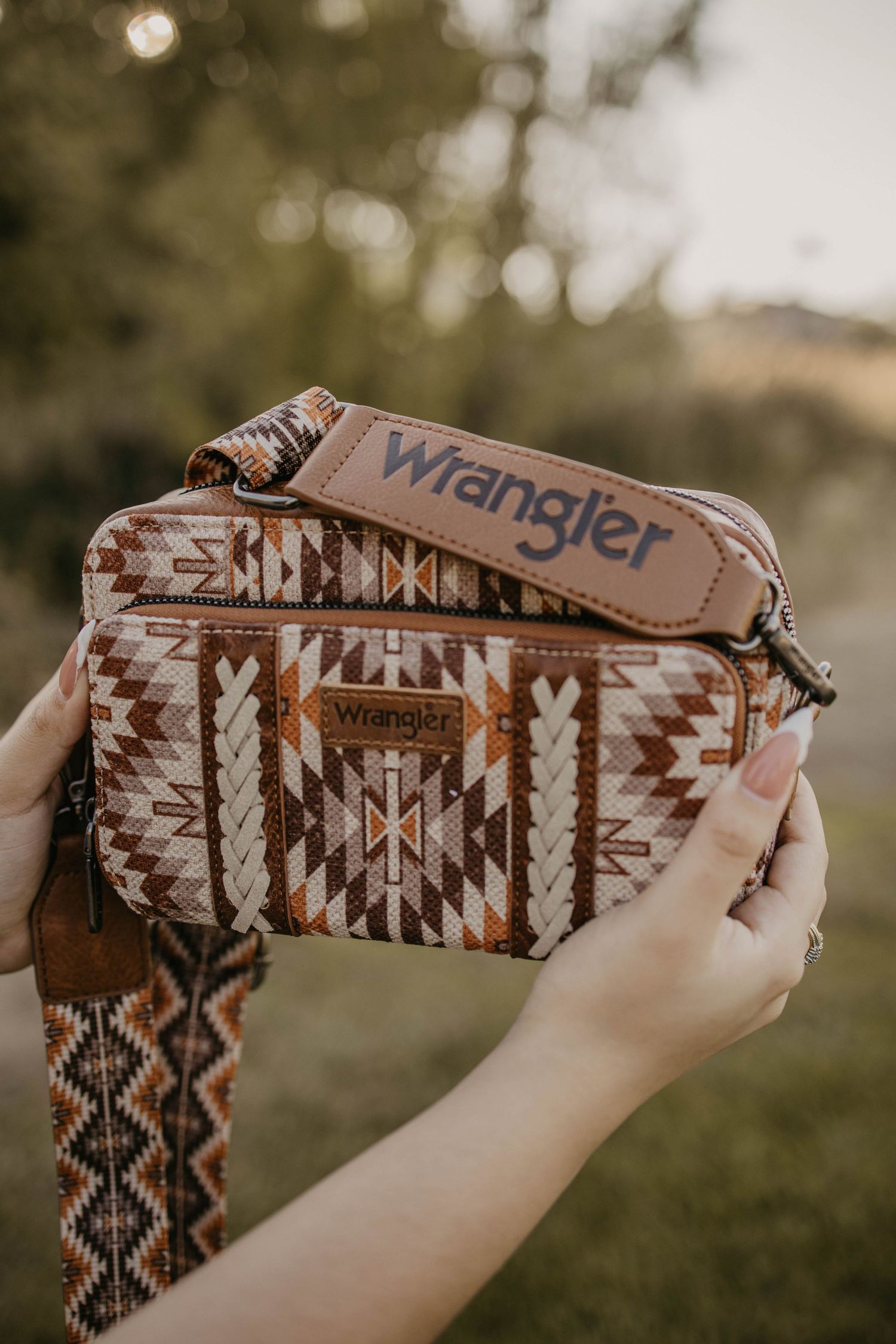Wrangler branded wallet with brown and white aztec pattern held against blurred outdoor background.