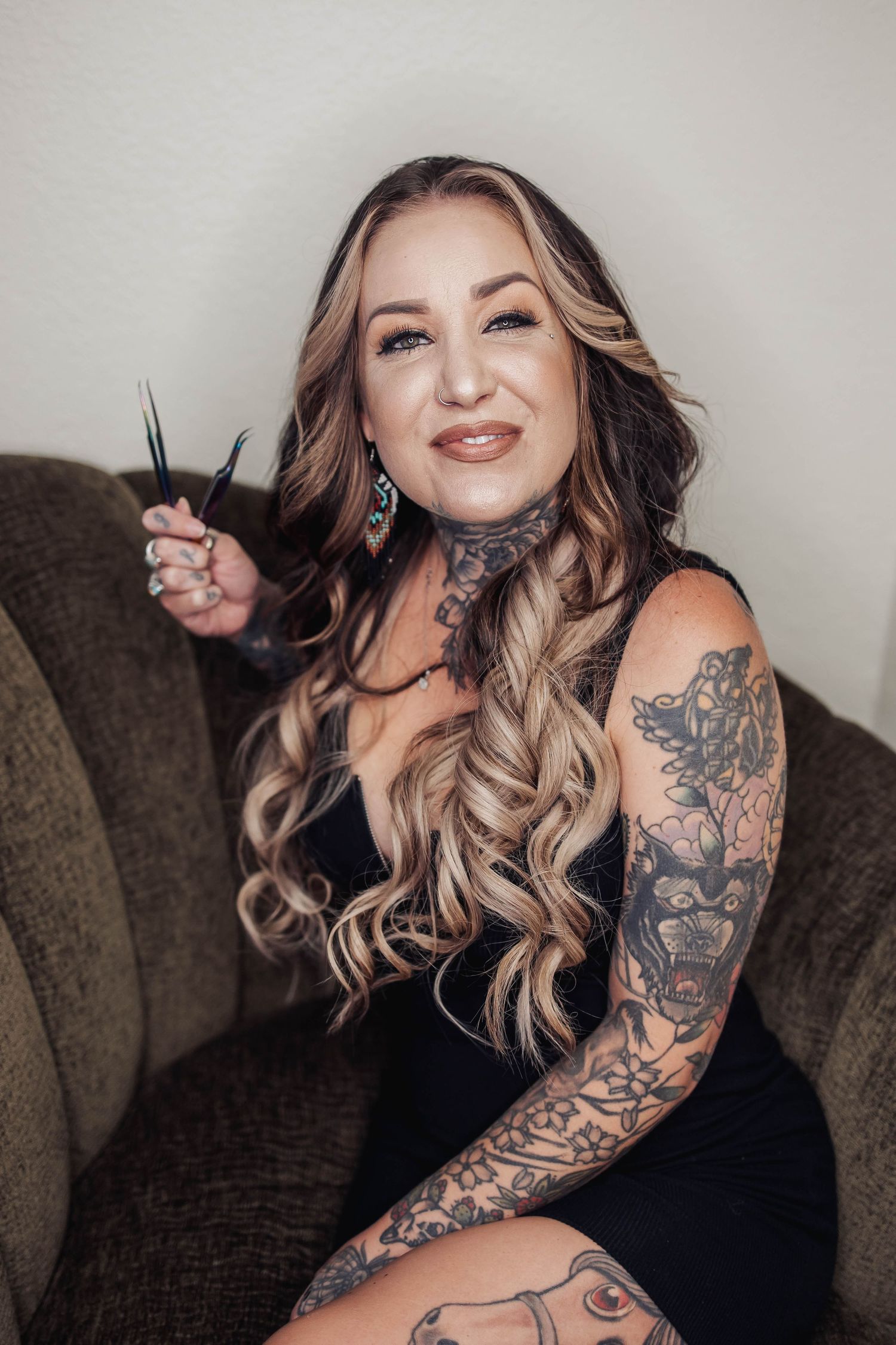 Person in black dress with tattoos posing on brown couch.